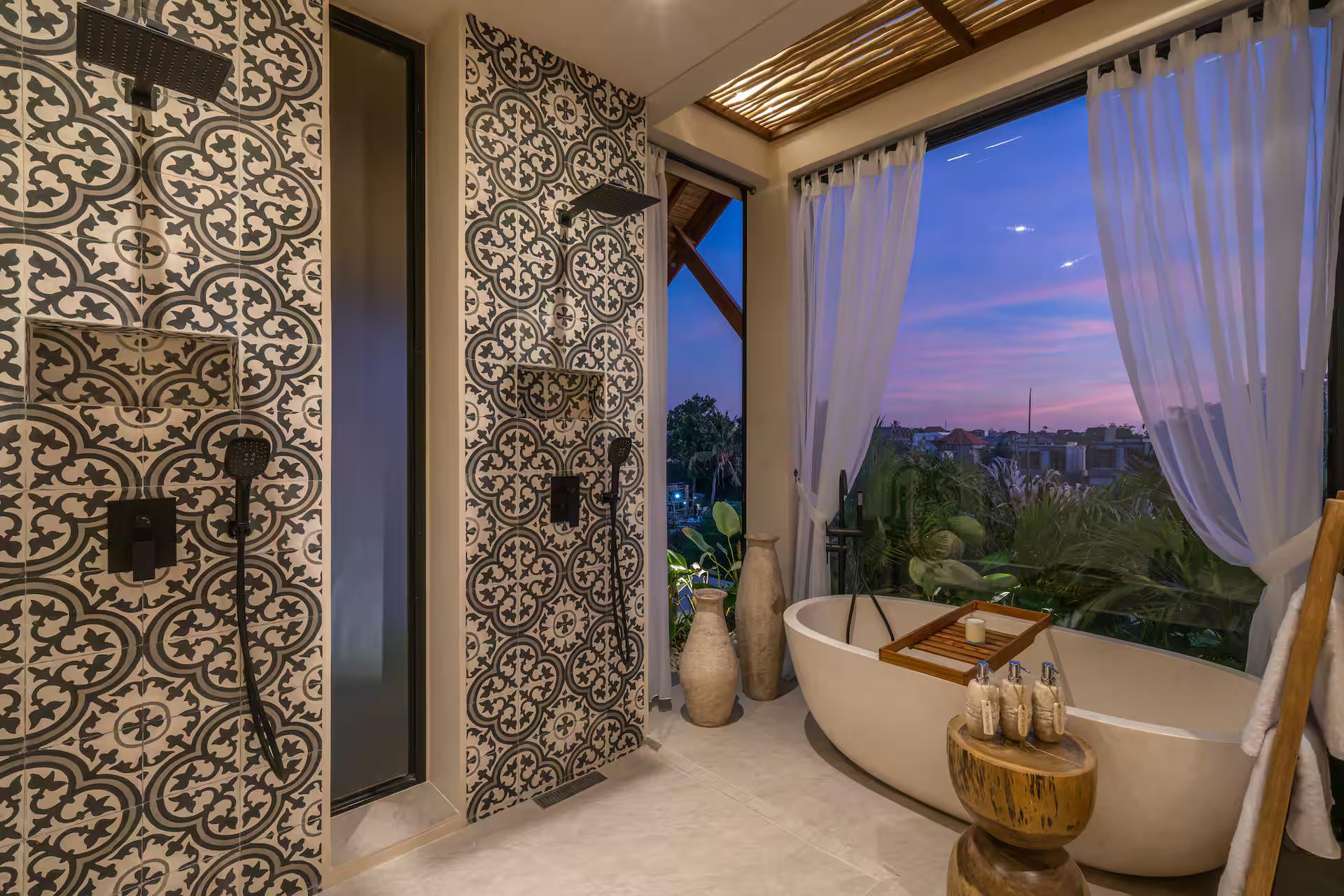 En-suite at dusk with twin rain showers on patterned cement tile and a freestanding oval tub