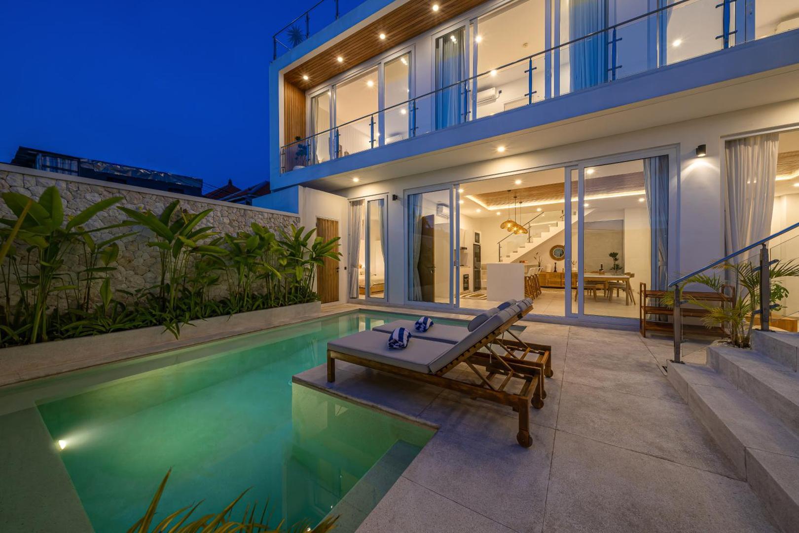 Villa Era lit across three floors at dusk, the pool green in front of the open living room