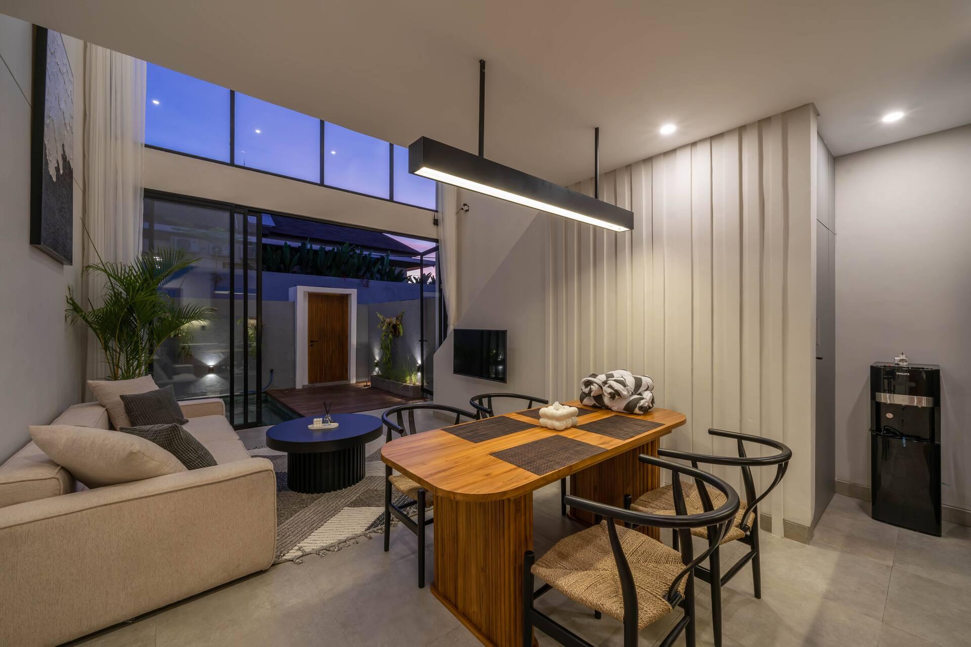 Timber dining table and black-framed chairs under a linear pendant, courtyard lit at dusk