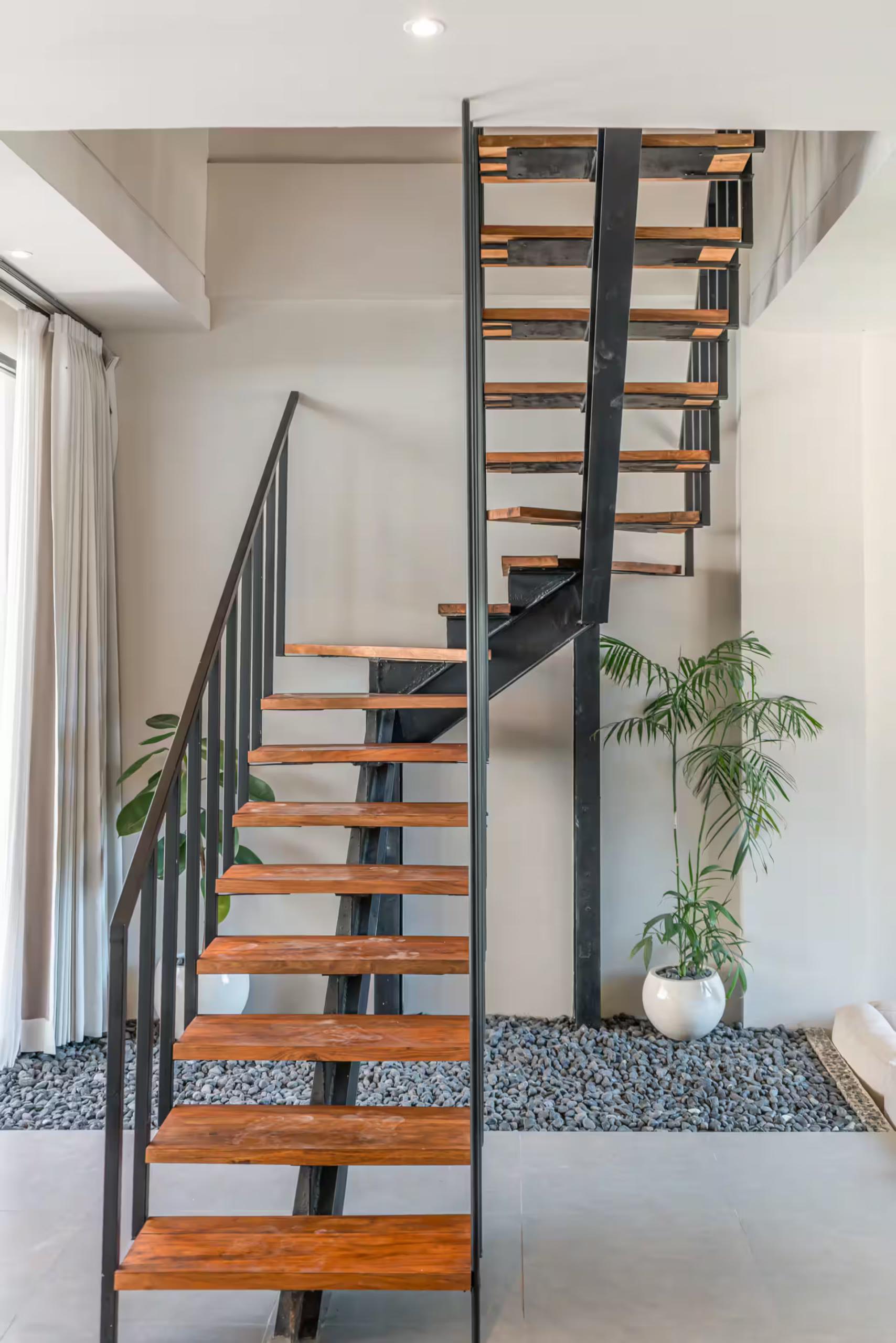 Open-tread timber staircase at Salt Villa, rising from a bed of river pebbles