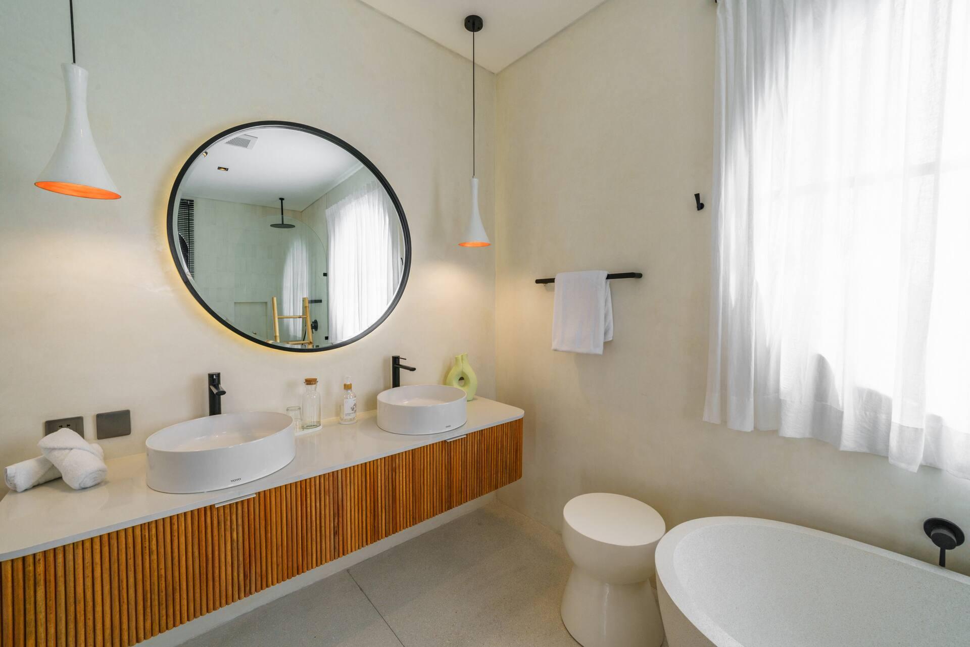 Freestanding oval bath and a fluted timber vanity under a round mirror in pale microcement