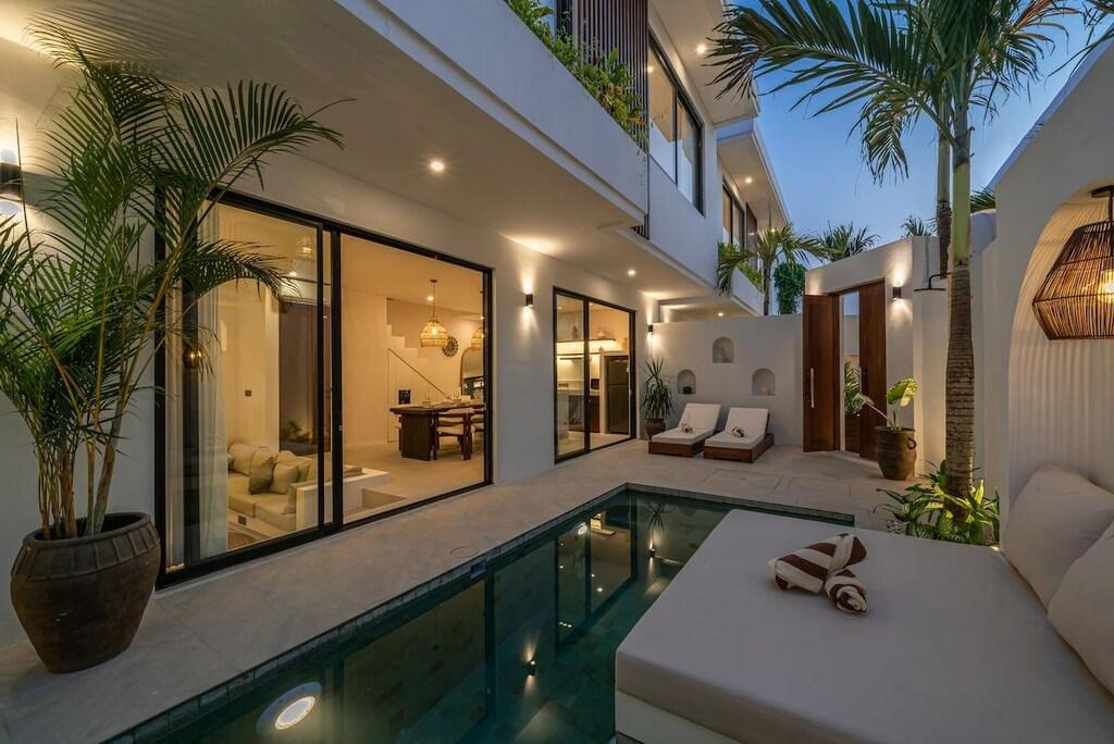 The poolside daybed at dusk, lanterns and underwater lights on across the courtyard