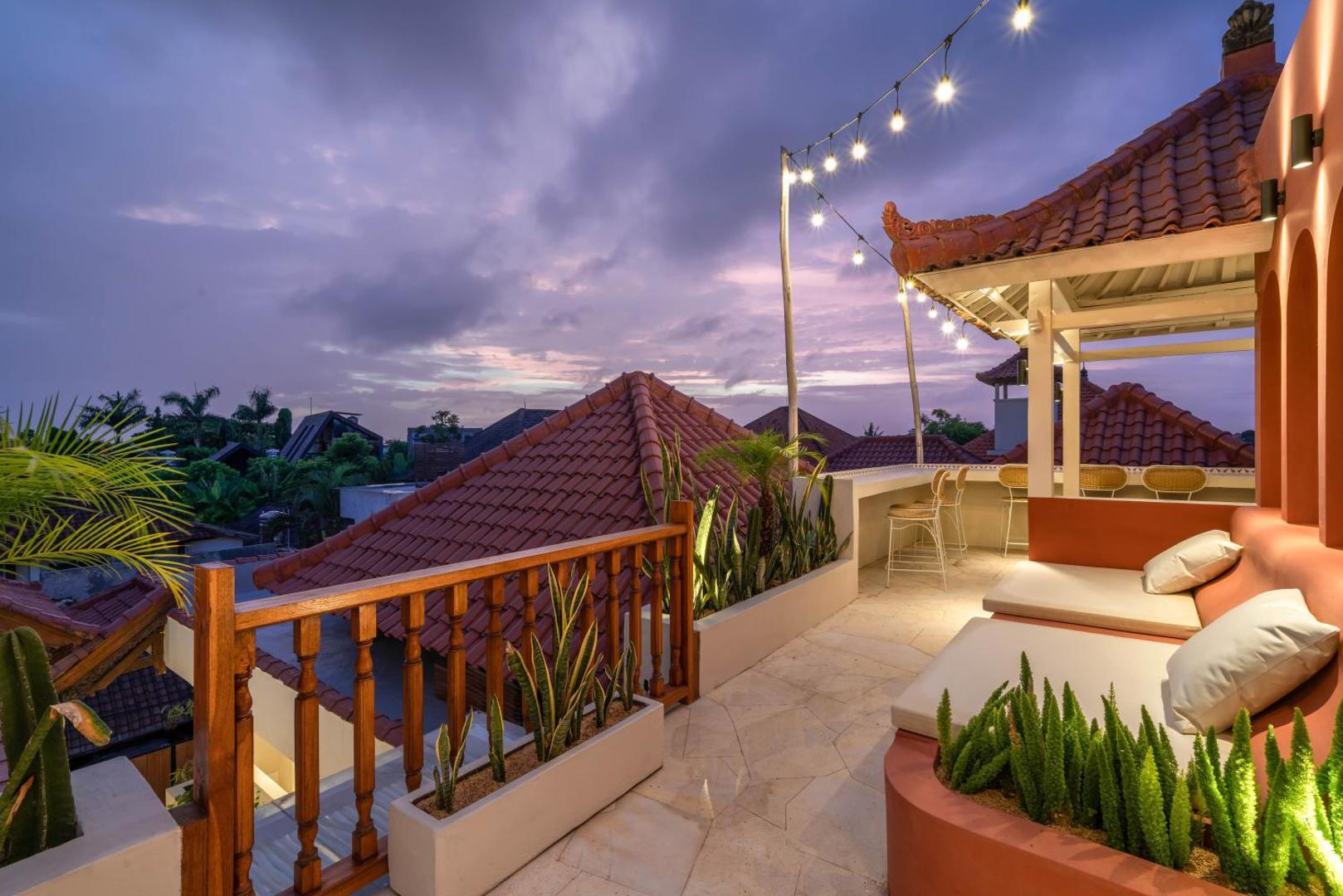 Dusk on the rooftop terrace, string lights strung above the banquettes and red clay roofs