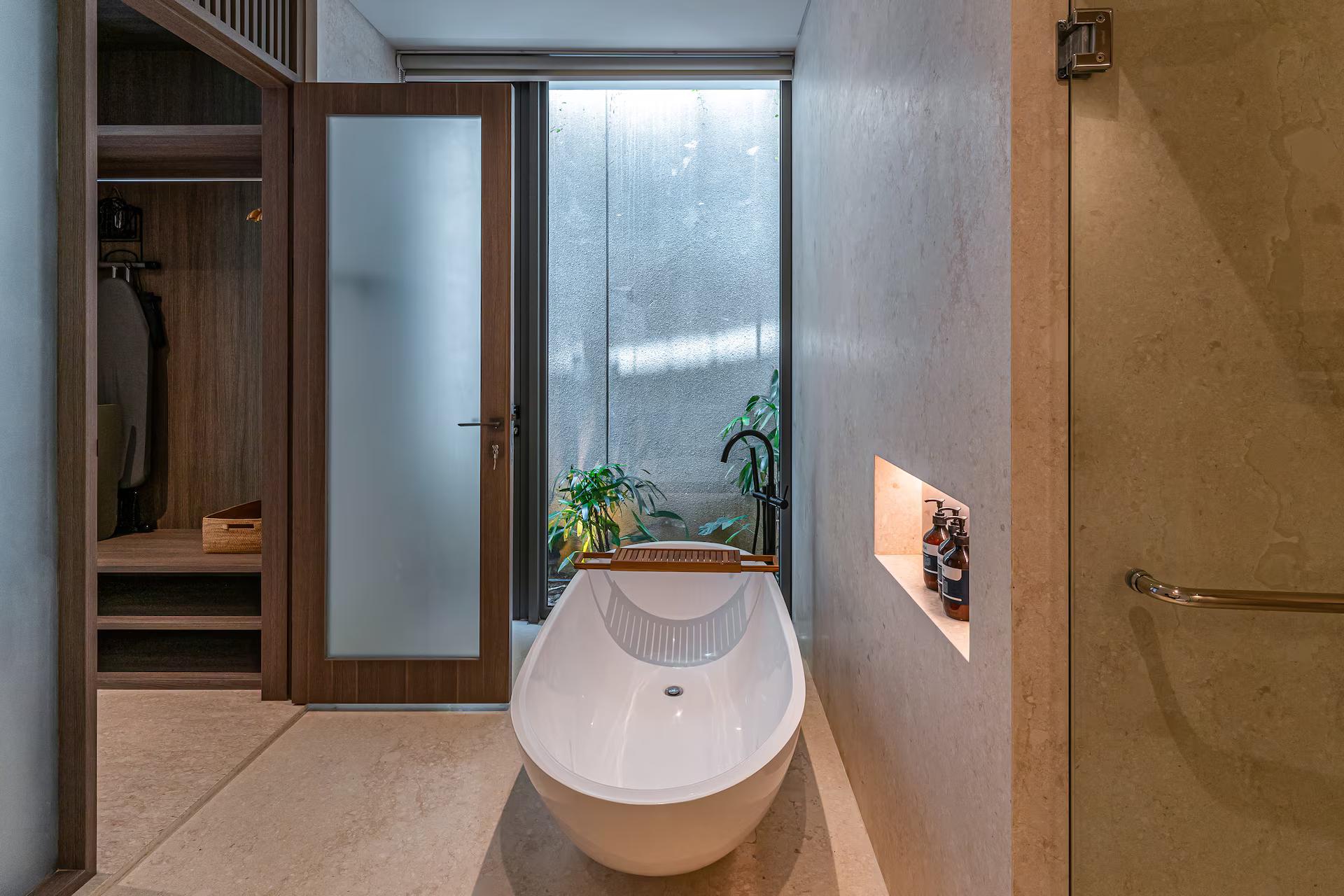 Freestanding stone bath set beside a planted light well in a master suite