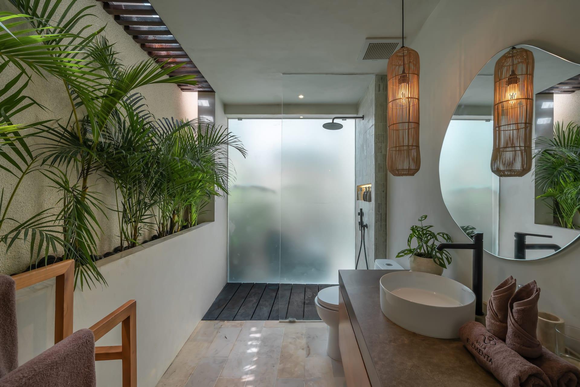 Bathroom with a stone vessel basin, round rattan-lit mirror and a glass-screened rain shower