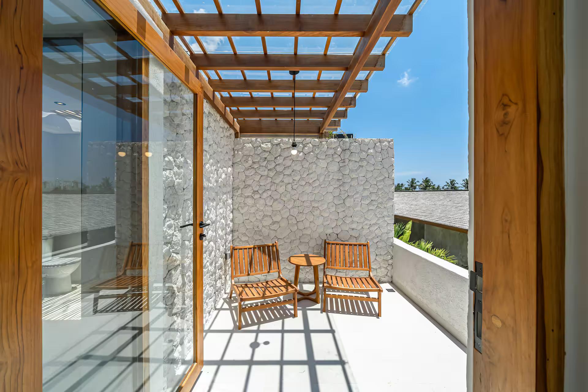 Upstairs balcony with a timber-slat pergola against a wall of coral stone