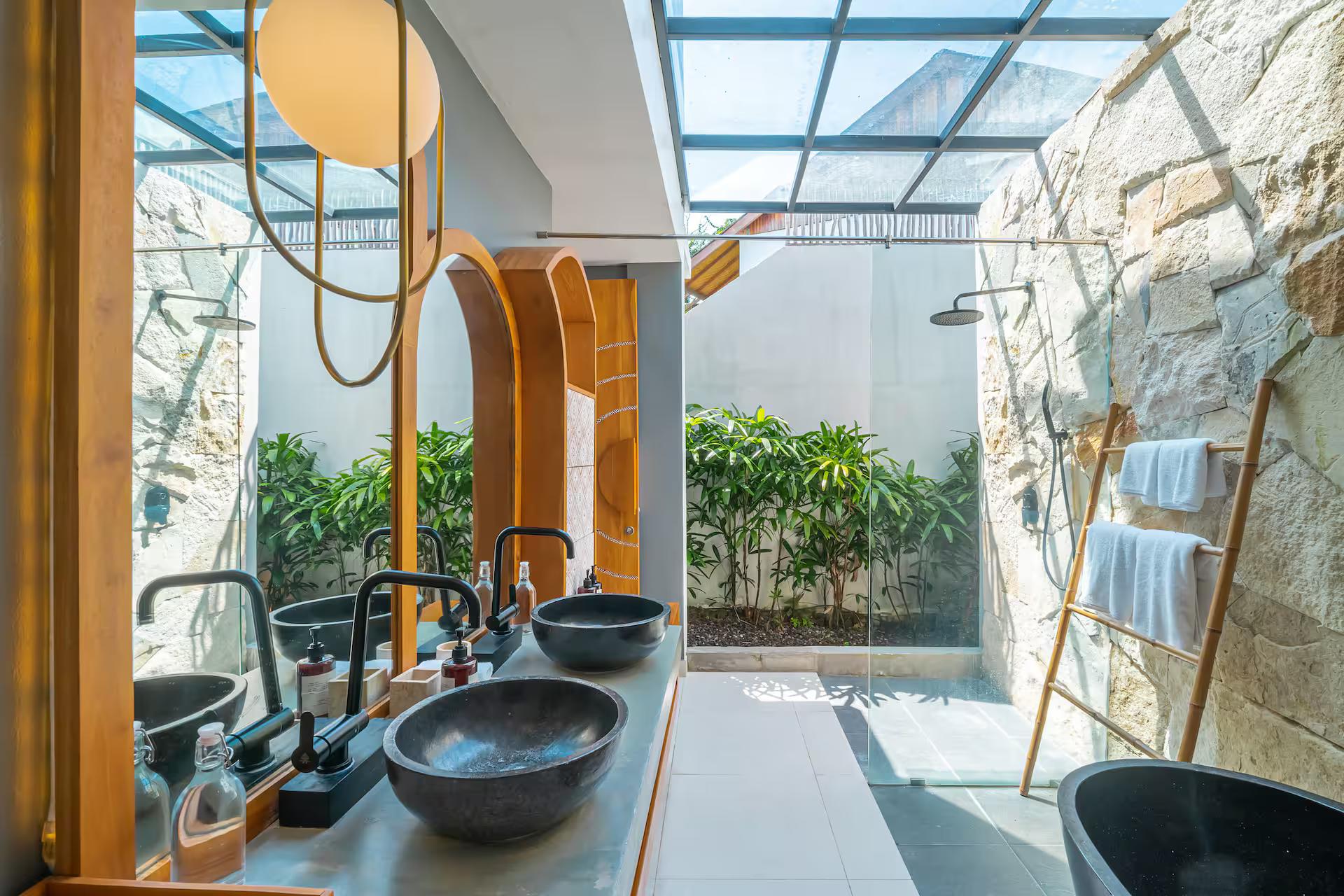 Bathroom open to the sky under glass, twin black stone basins on a concrete slab beside ferns