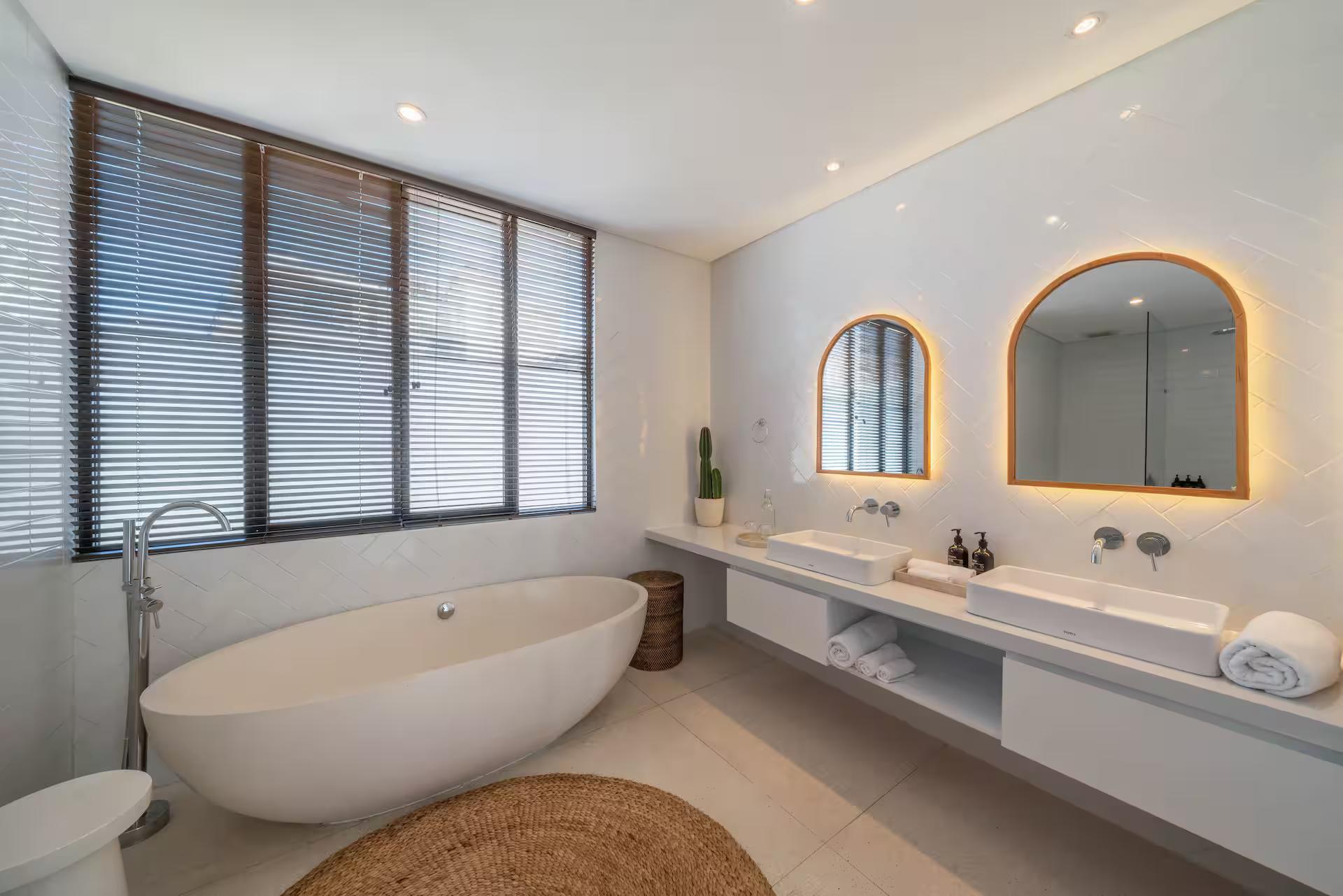 A freestanding oval tub under louvred windows, twin arched mirrors above a double vanity