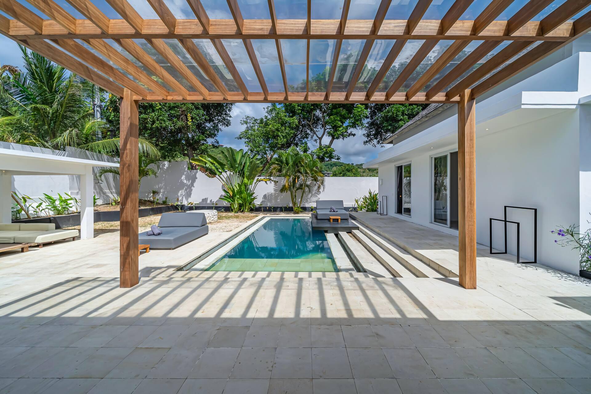 Timber pergola casting striped shade over the pool terrace and sun-bleached stone steps