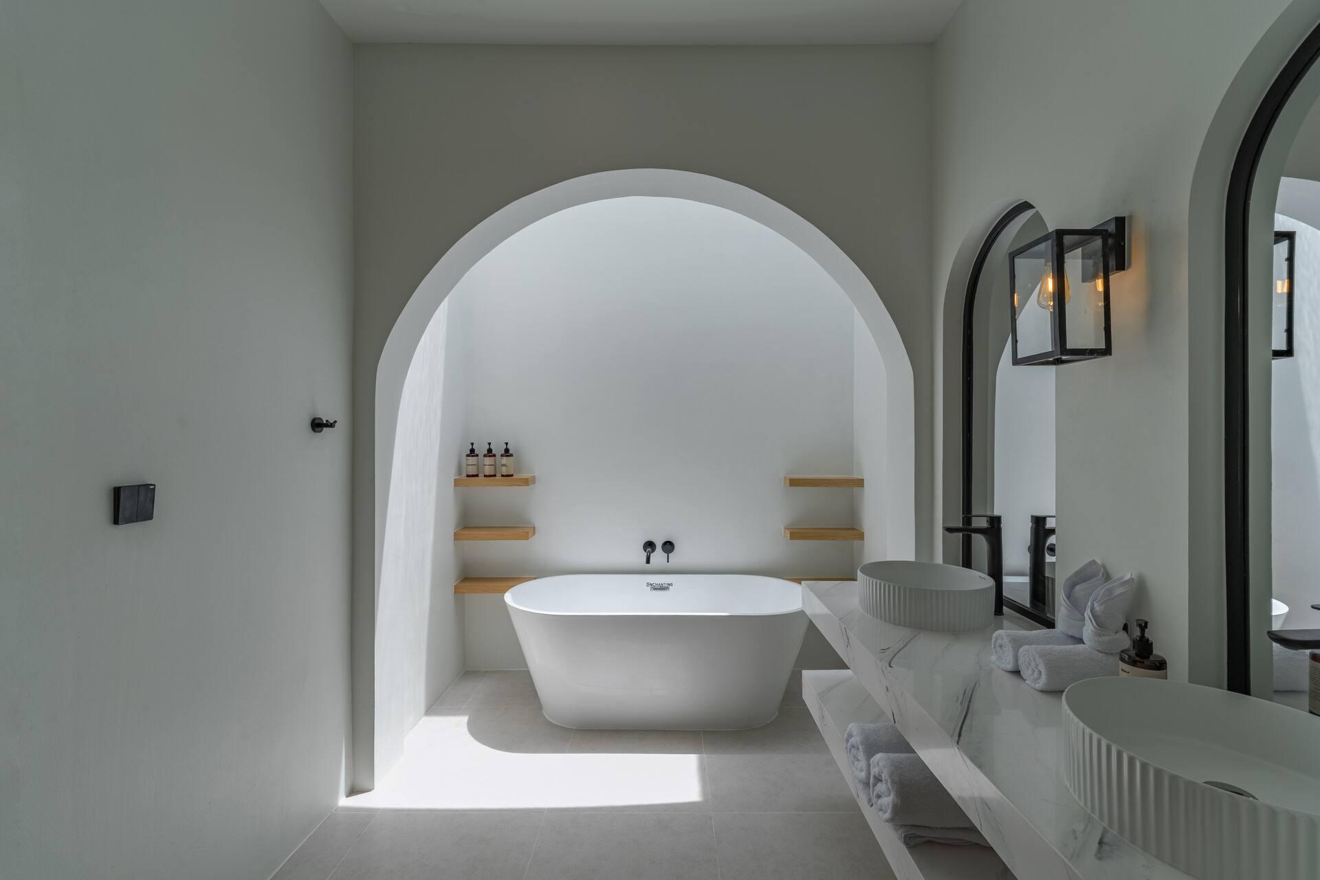 Freestanding bath set into a white arched alcove, with a stone vanity and black lantern wall lights