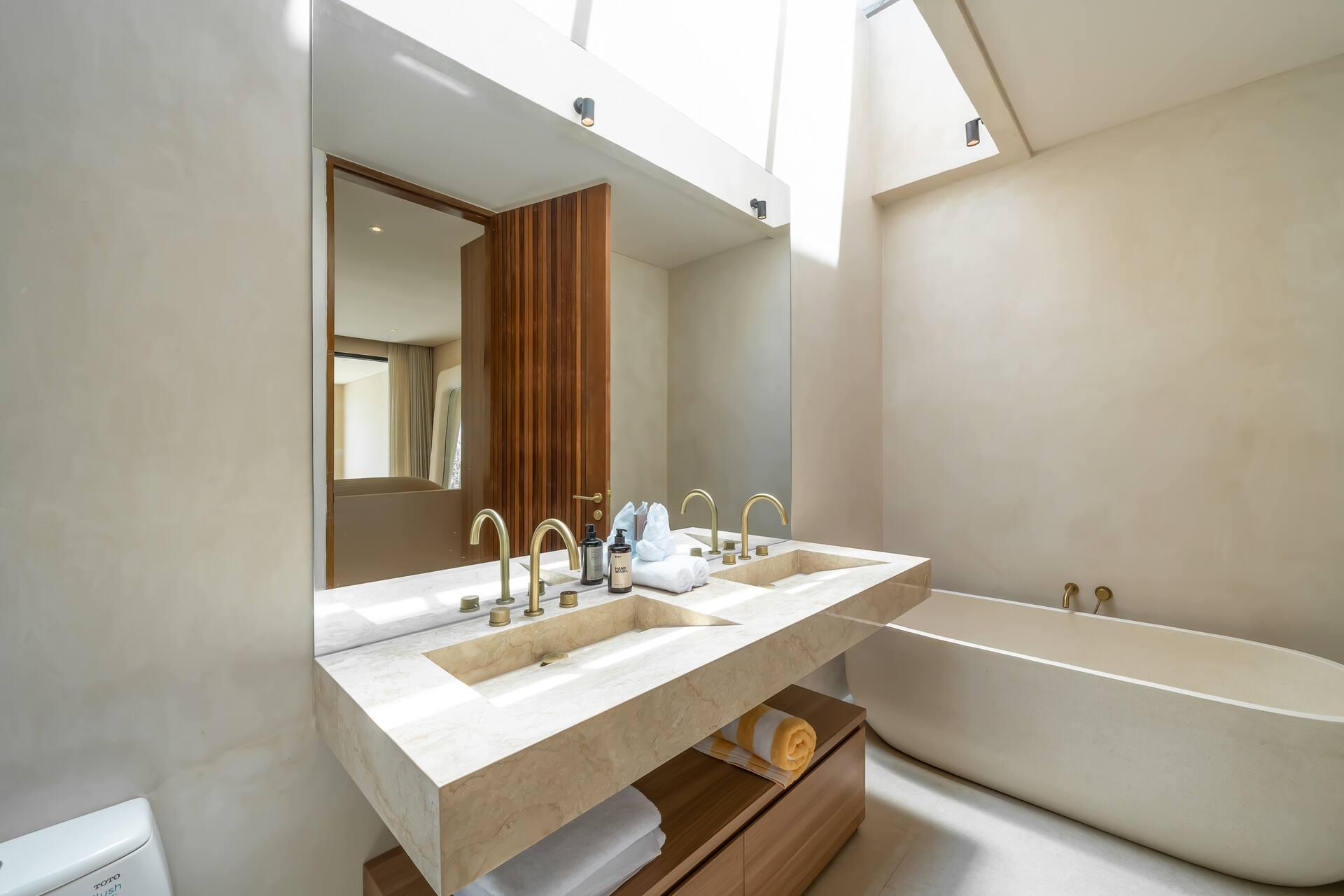 Travertine-toned bathroom with a carved stone basin, brushed brass taps and a freestanding stone bath