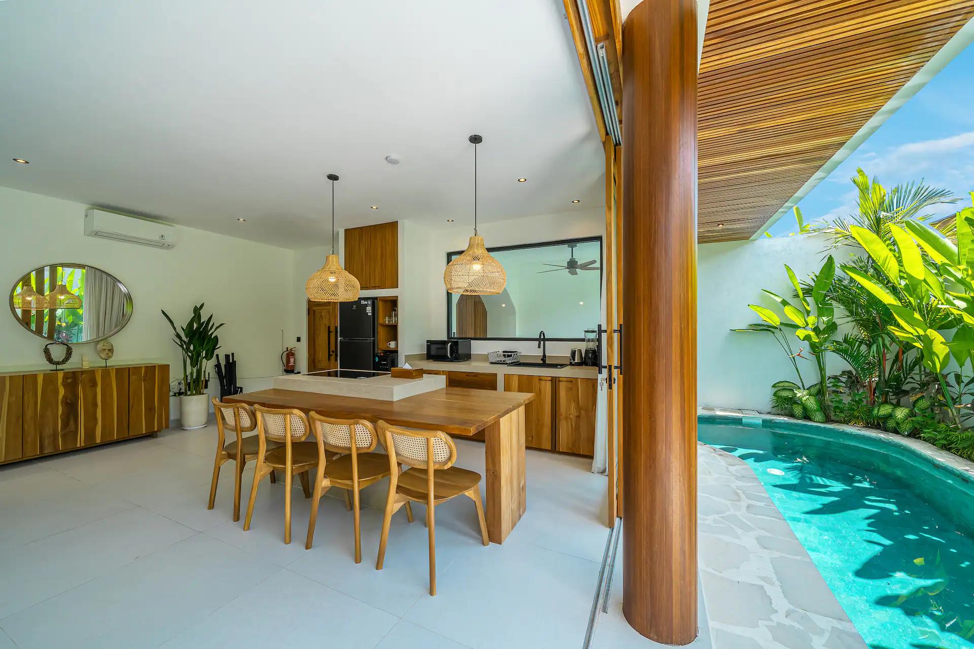 Dining table for six in pale timber beside the kitchen island, pool through the opening