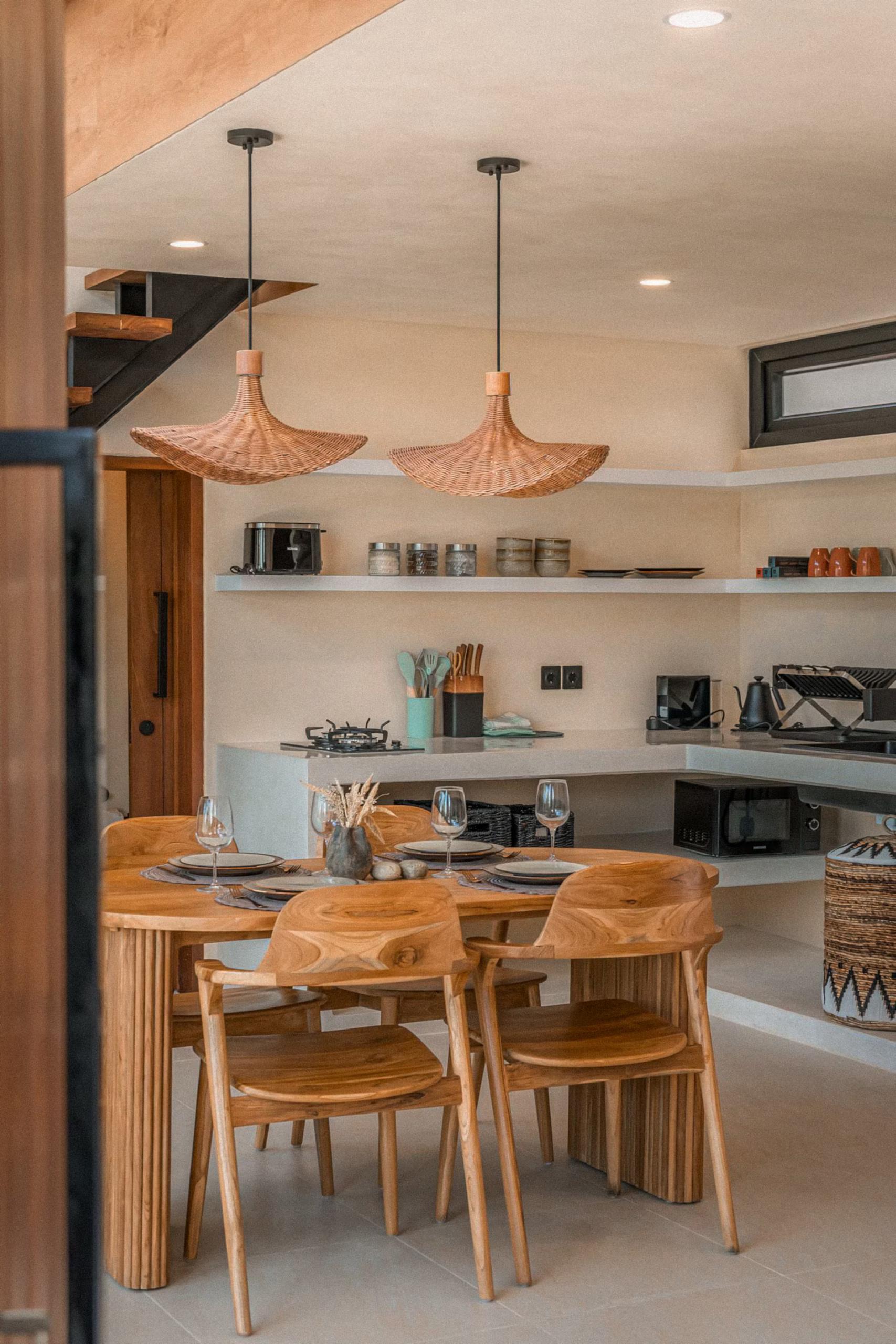 Oval teak dining table and curved chairs beneath copper-toned woven pendants