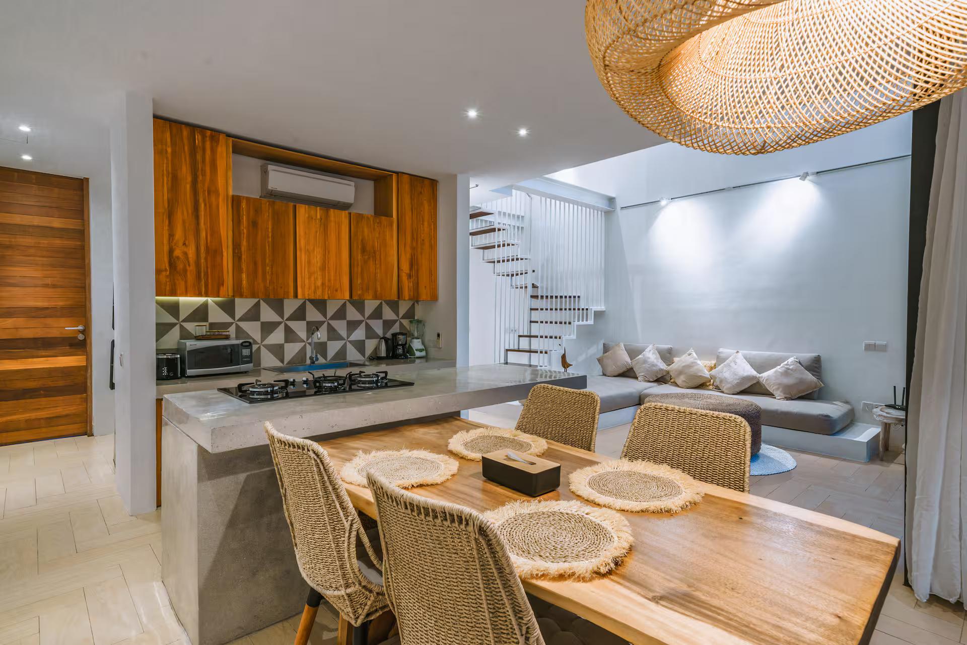 Timber dining table and concrete kitchen island under an oversized woven rattan pendant