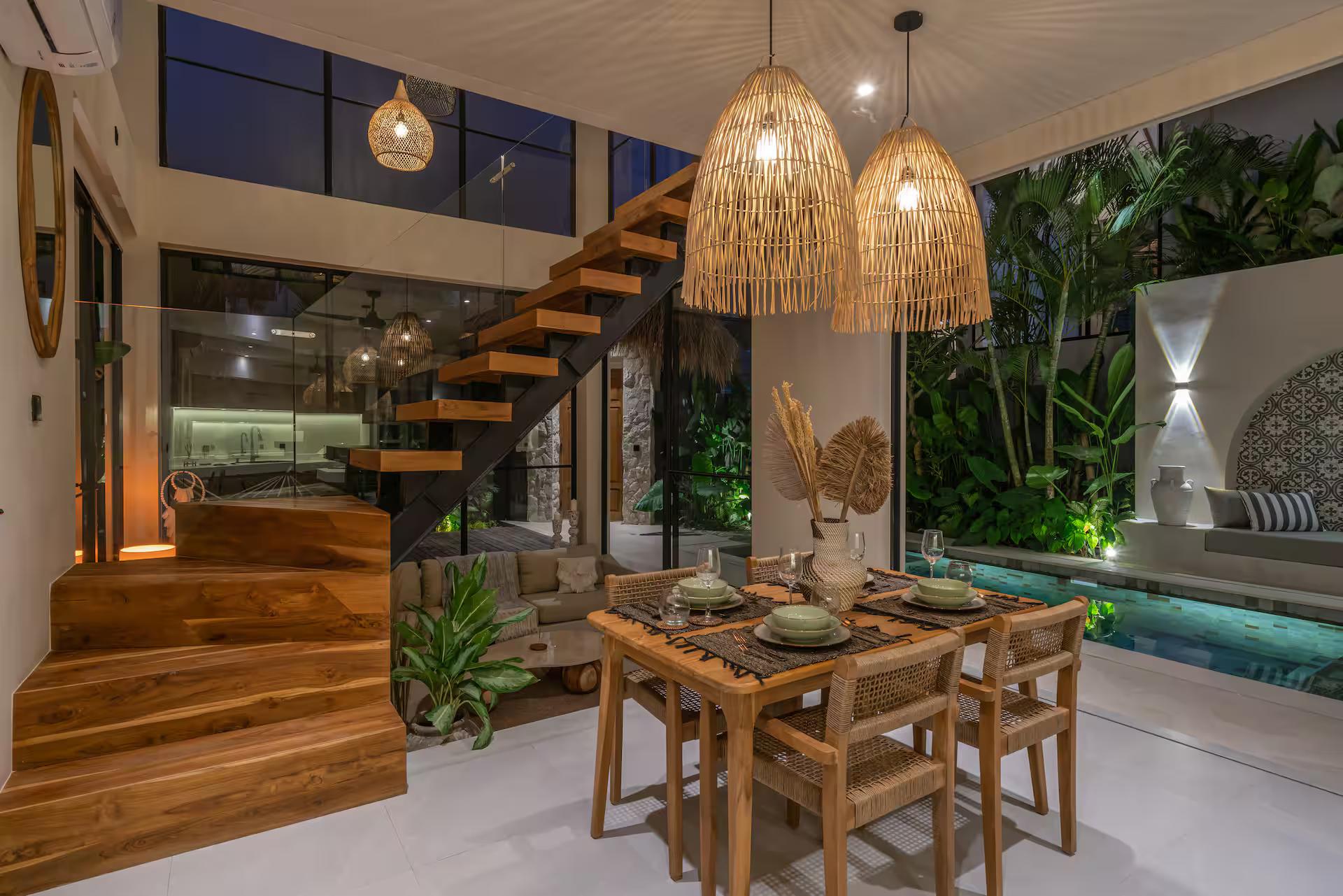 Dining table for six beside the timber staircase, glass doors open to the pool at Villa Saya