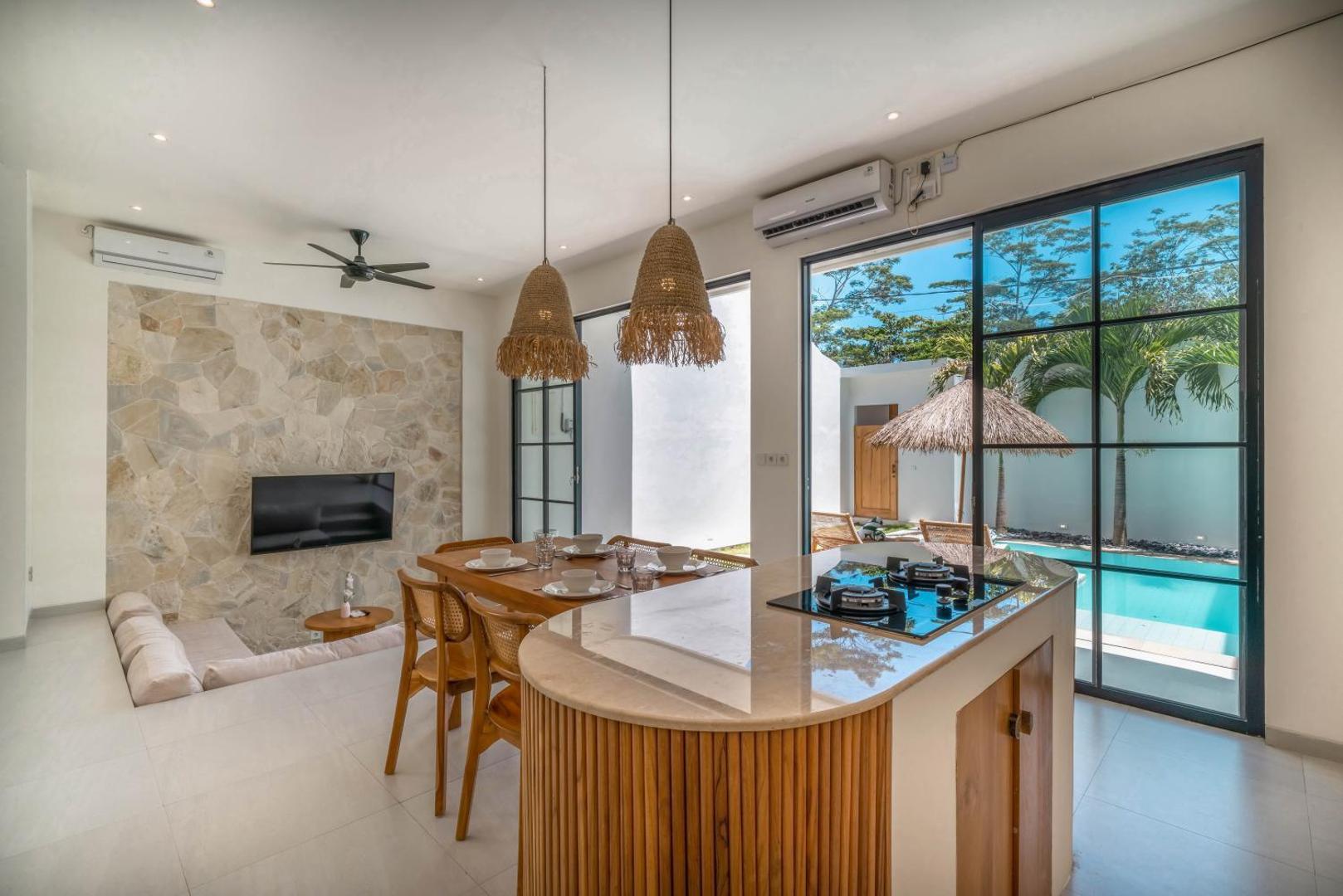 Curved travertine kitchen island on a fluted timber base, dining table just beyond