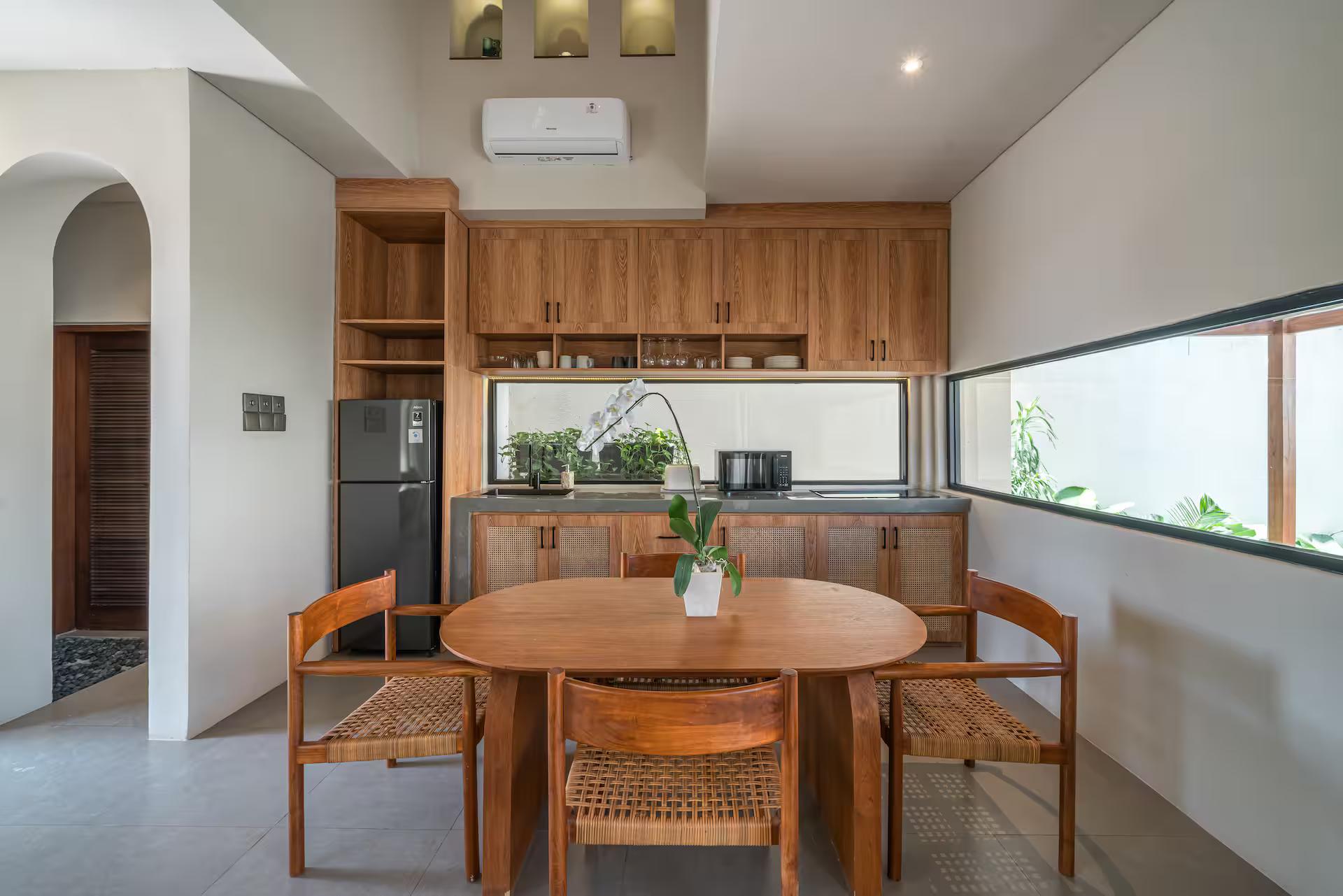 Round timber dining table with rattan chairs beside the kitchen joinery at Salt Villa