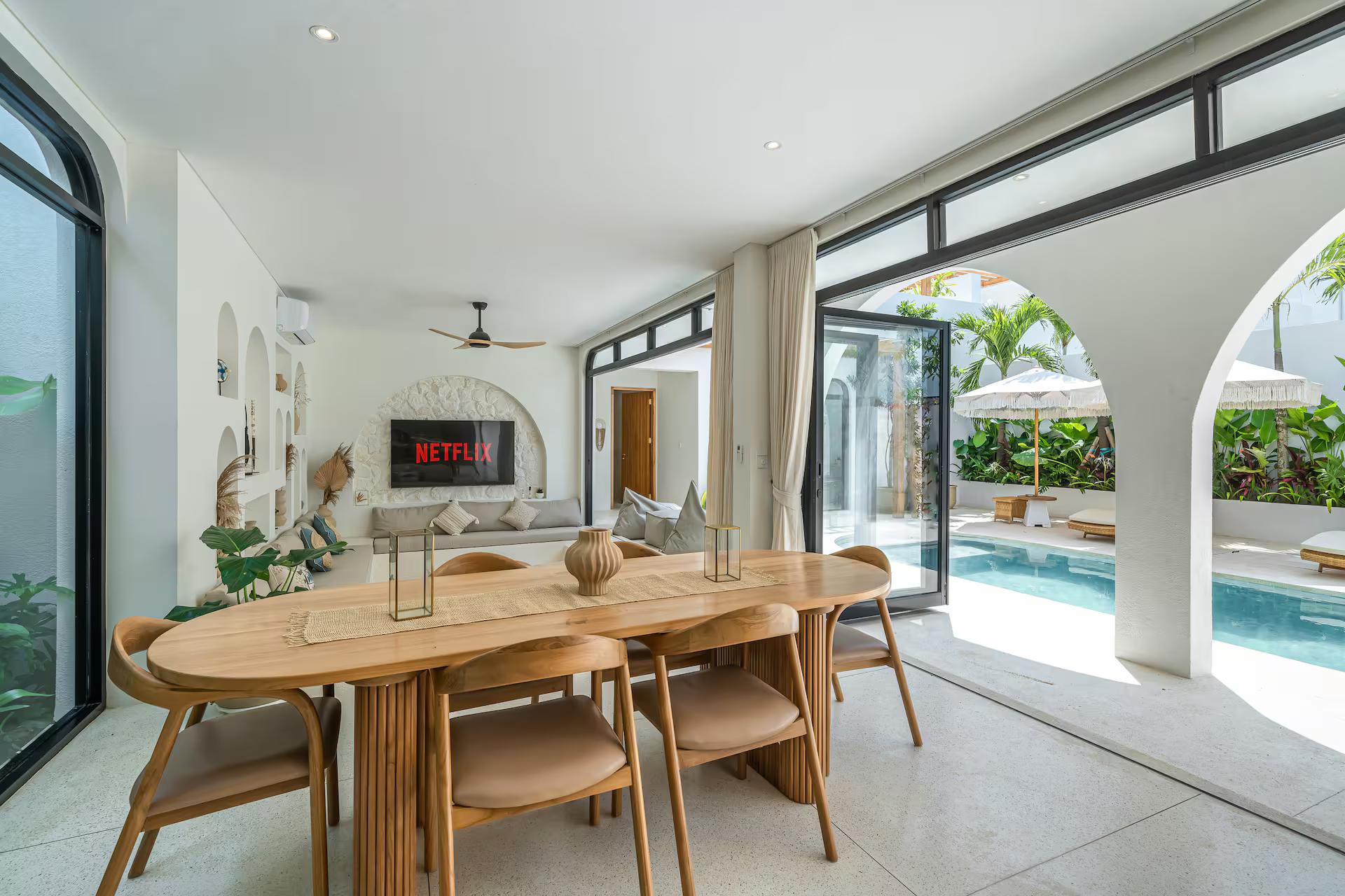 Oval dining table for six under woven pendants, the pool visible through the glass