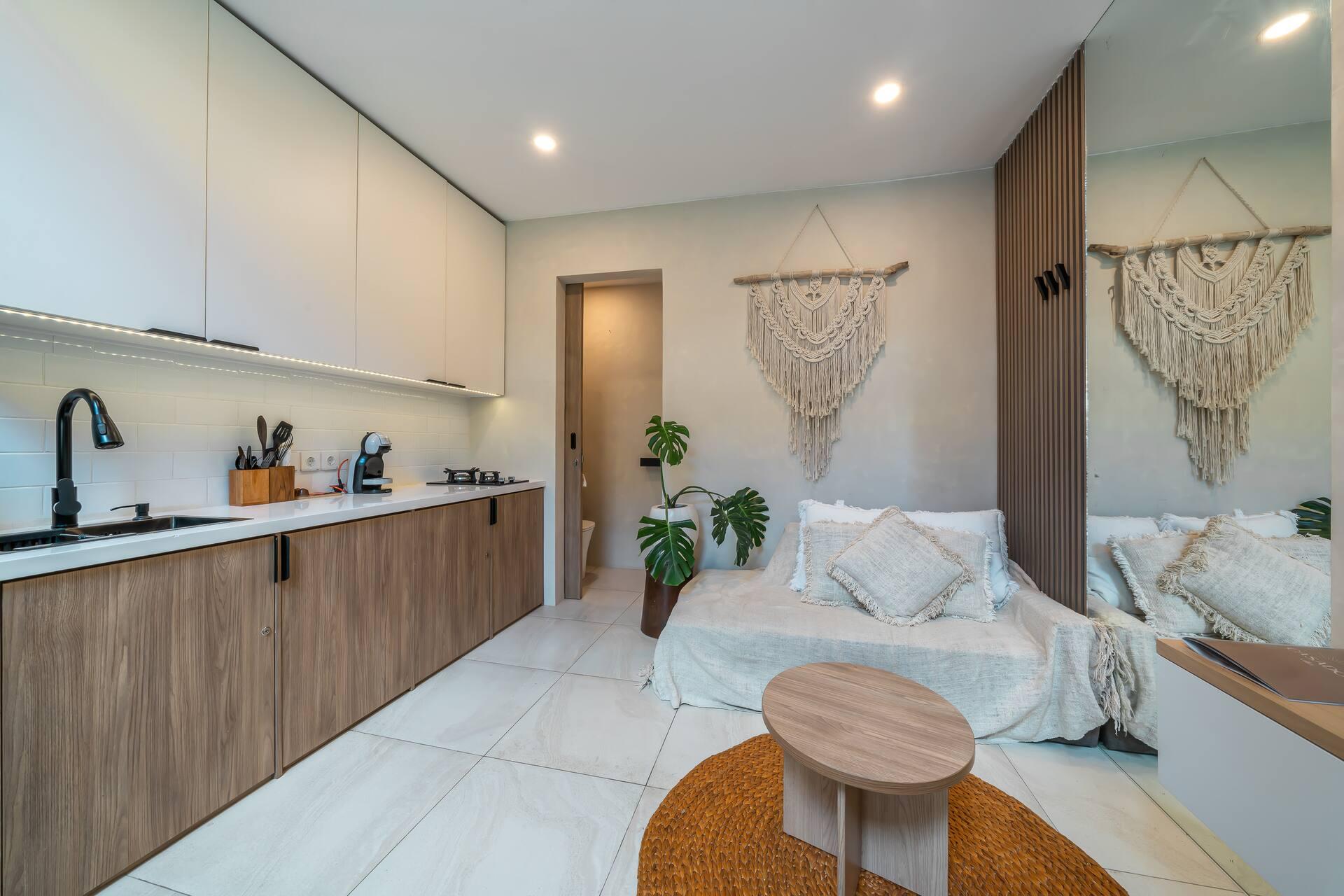 Kitchenette in warm timber facing a low daybed under a macrame on a driftwood rod