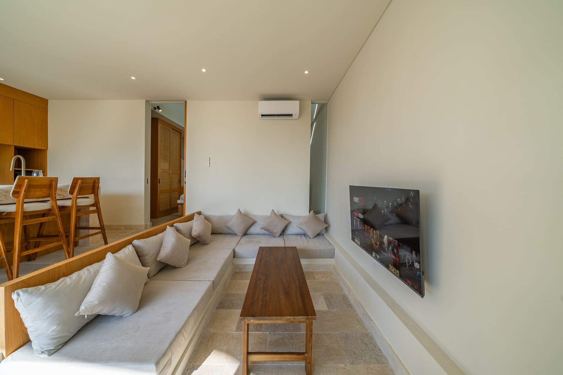 Long linen banquette and low teak coffee table facing the wall-mounted television at Villa Amber