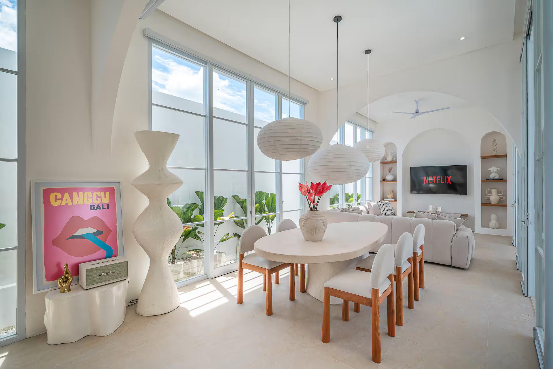 Round dining table under three rice-paper globes beside full-height glazing