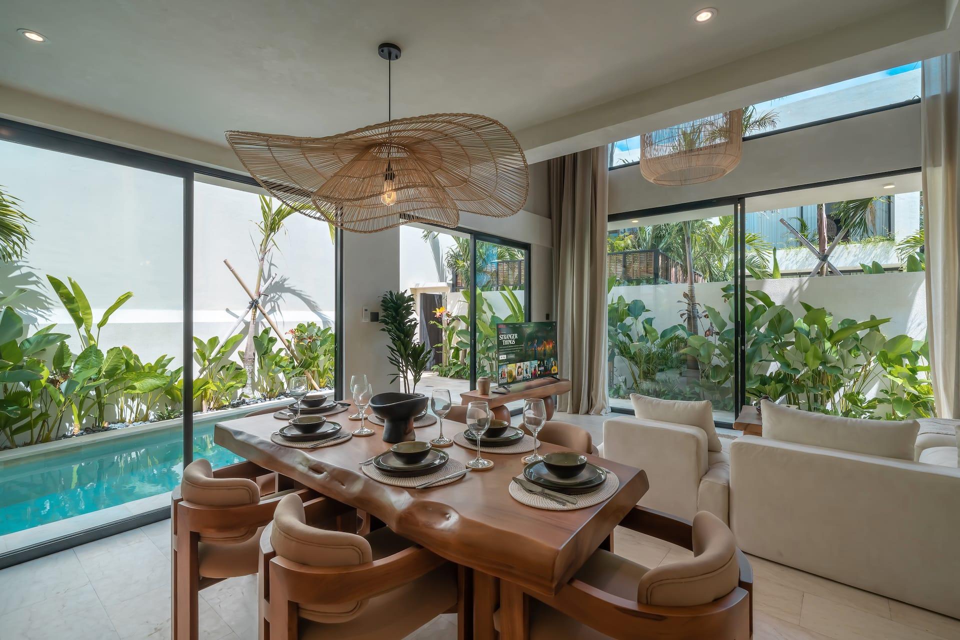Dining table for six beneath an oversized woven pendant, glazed wall onto the garden