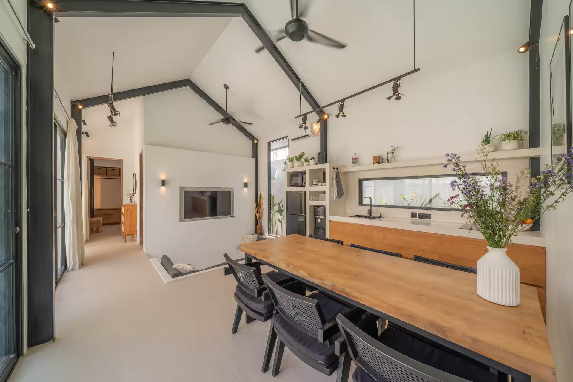 Long timber dining table with black mesh chairs beneath the trussed vaulted ceiling