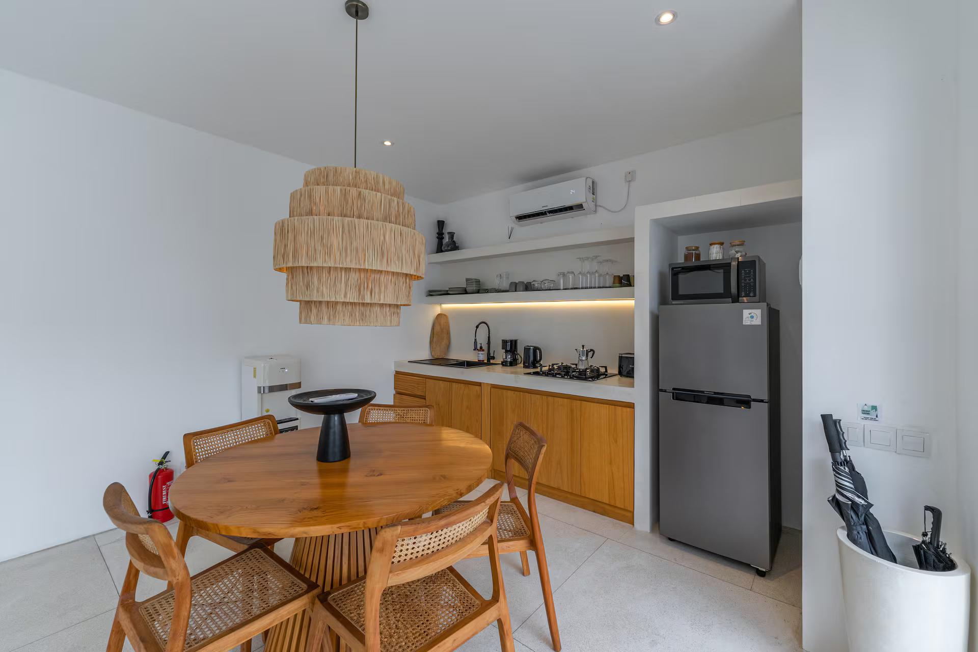 Round timber dining table and rattan chairs beside the open kitchen at Villa Valeria