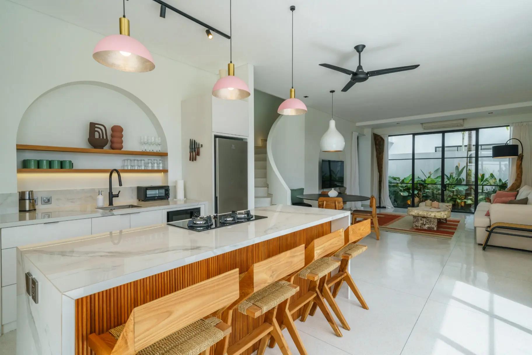 Marble kitchen island with a fluted timber front and bar stools under pink dome pendants