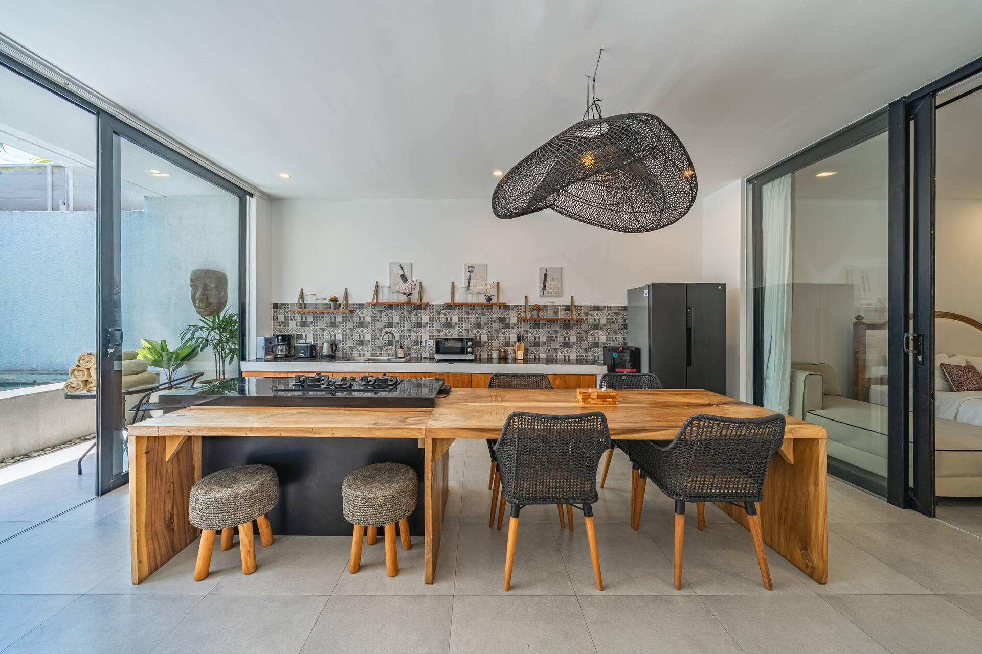 The kitchen island and timber dining table at Villa Athalla, doors folded back to the pool