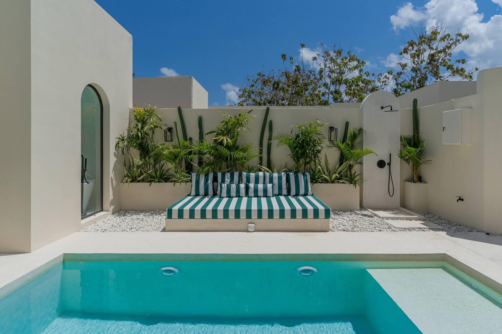 Striped daybed against a cactus-planted wall beside the pool, with an outdoor rain shower on the right