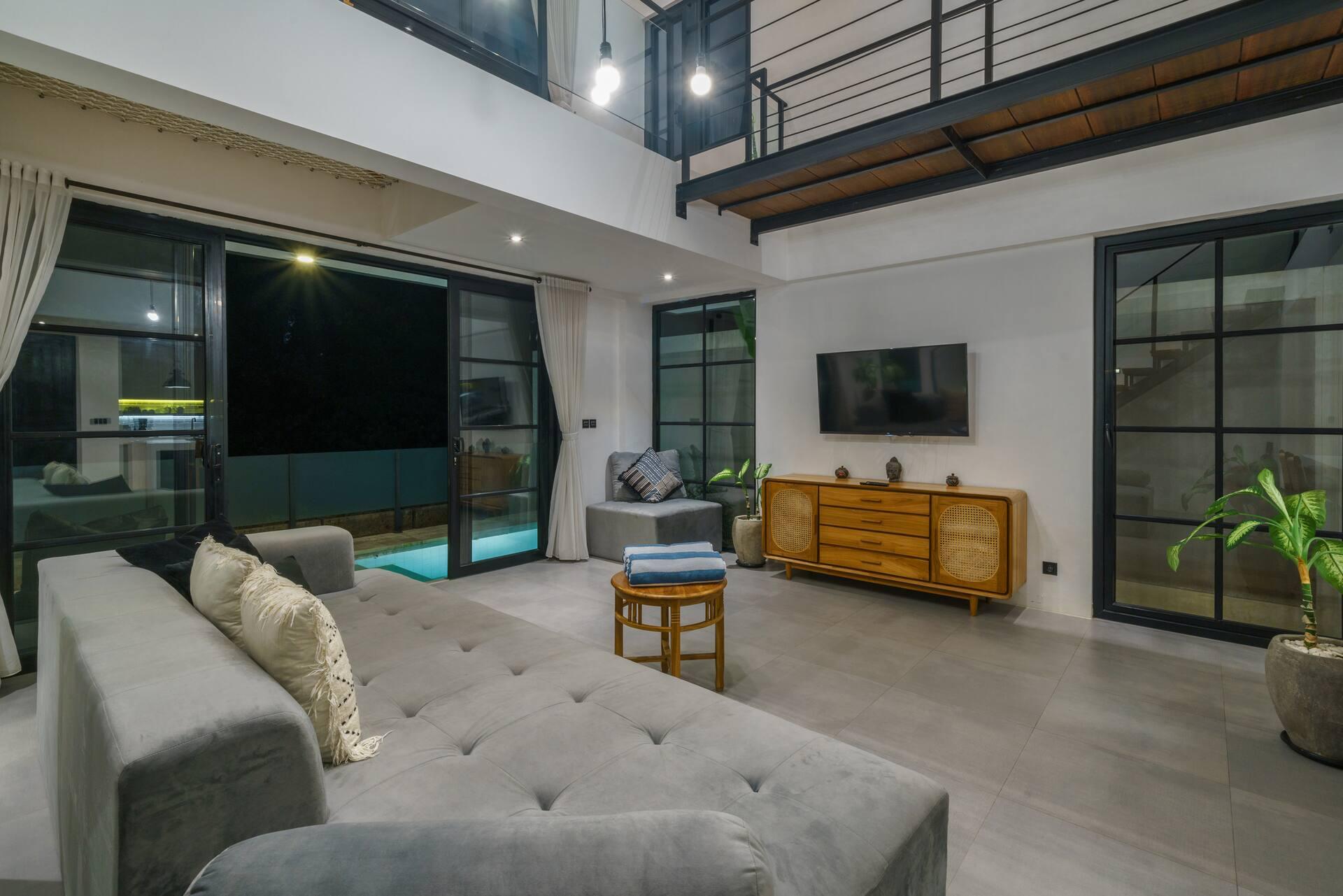 Grey tufted sofa facing full-height glass doors to the pool, with a rattan sideboard and TV