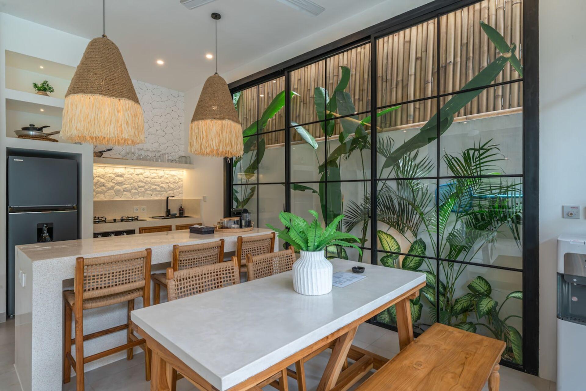 Timber dining table and rattan chairs under raffia pendants beside the kitchen
