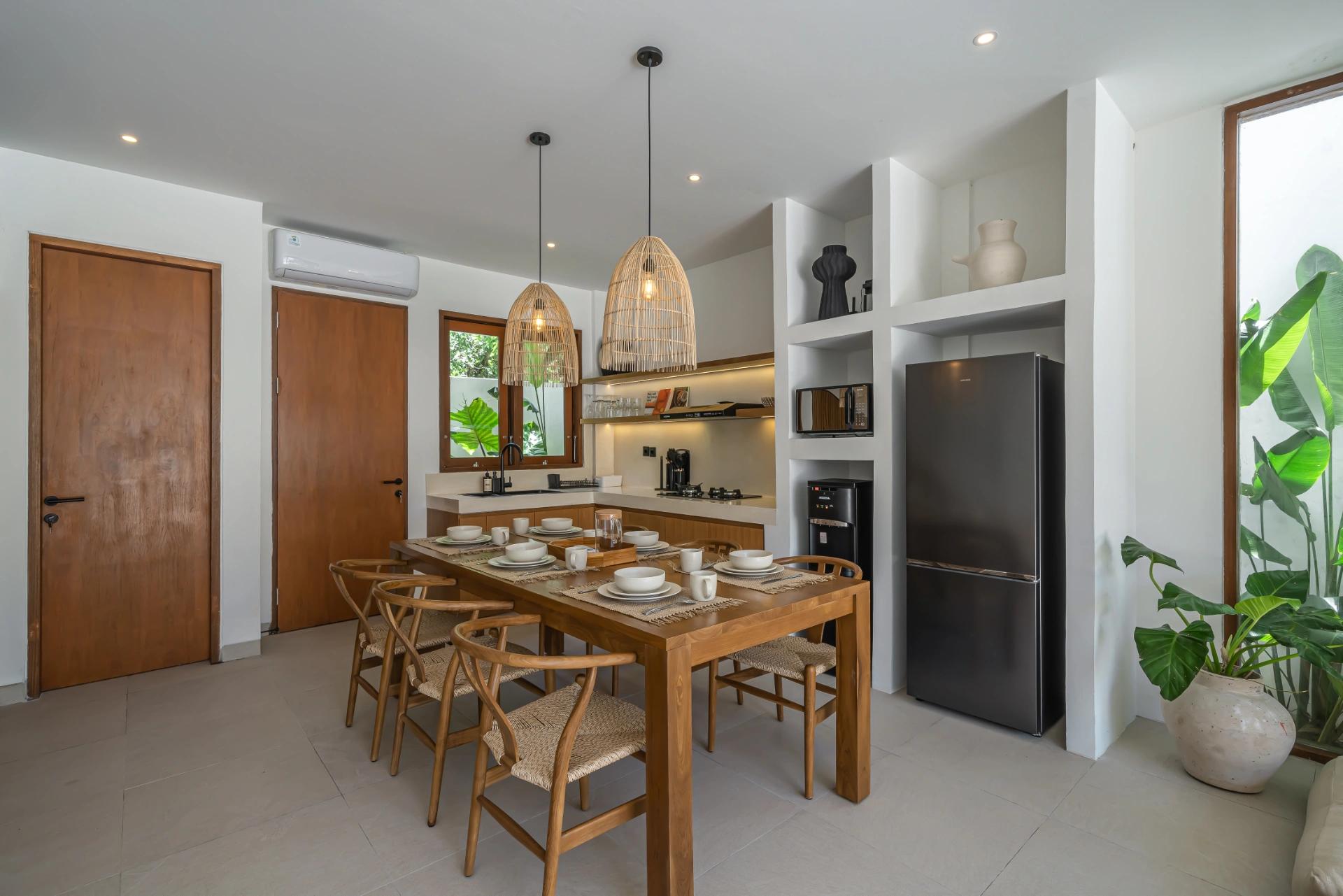 Teak dining table and woven-back chairs at Villa Kembali 10, kitchen and fridge behind