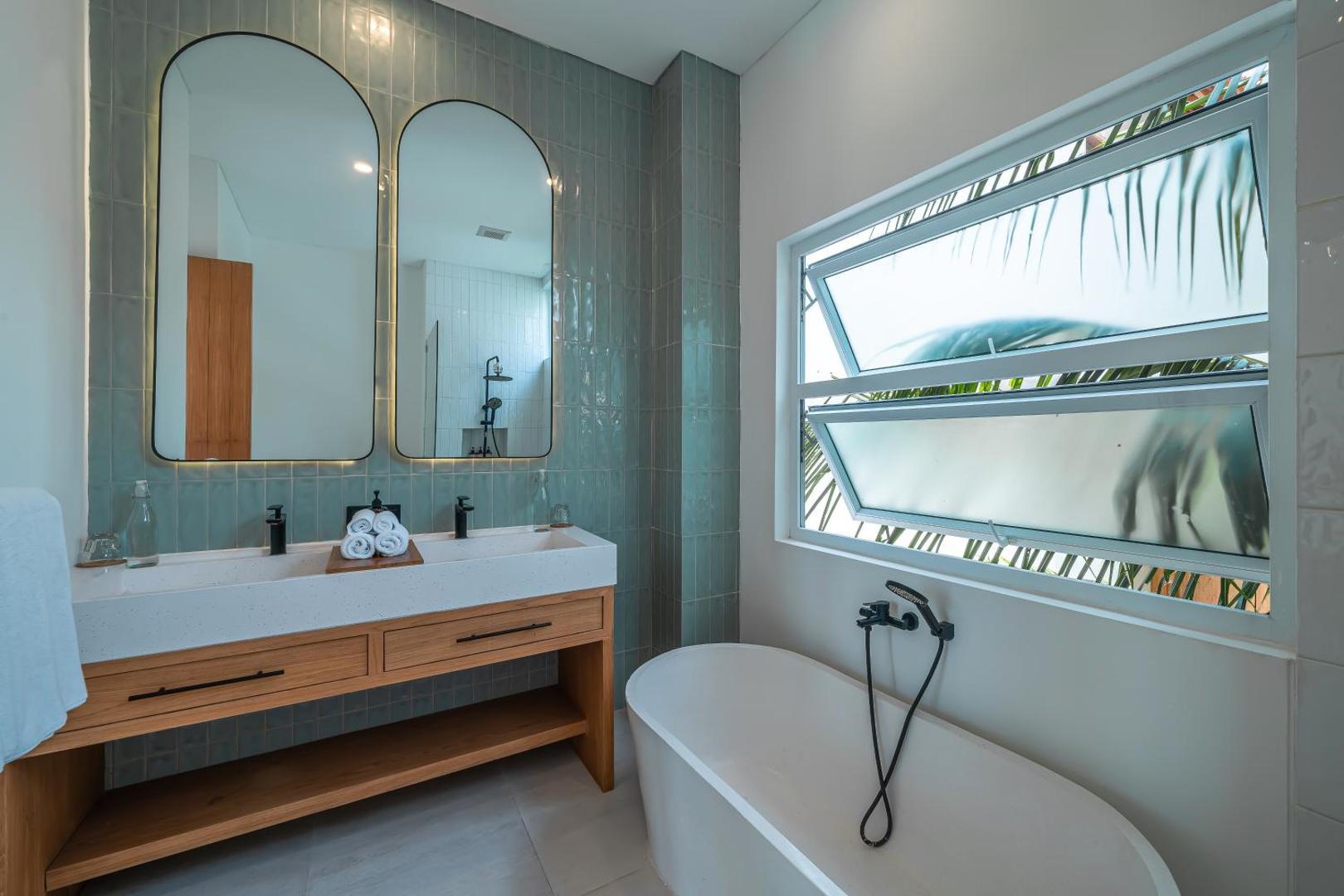 Bathroom at Villa Era with a freestanding tub, twin arched mirrors and a timber vanity