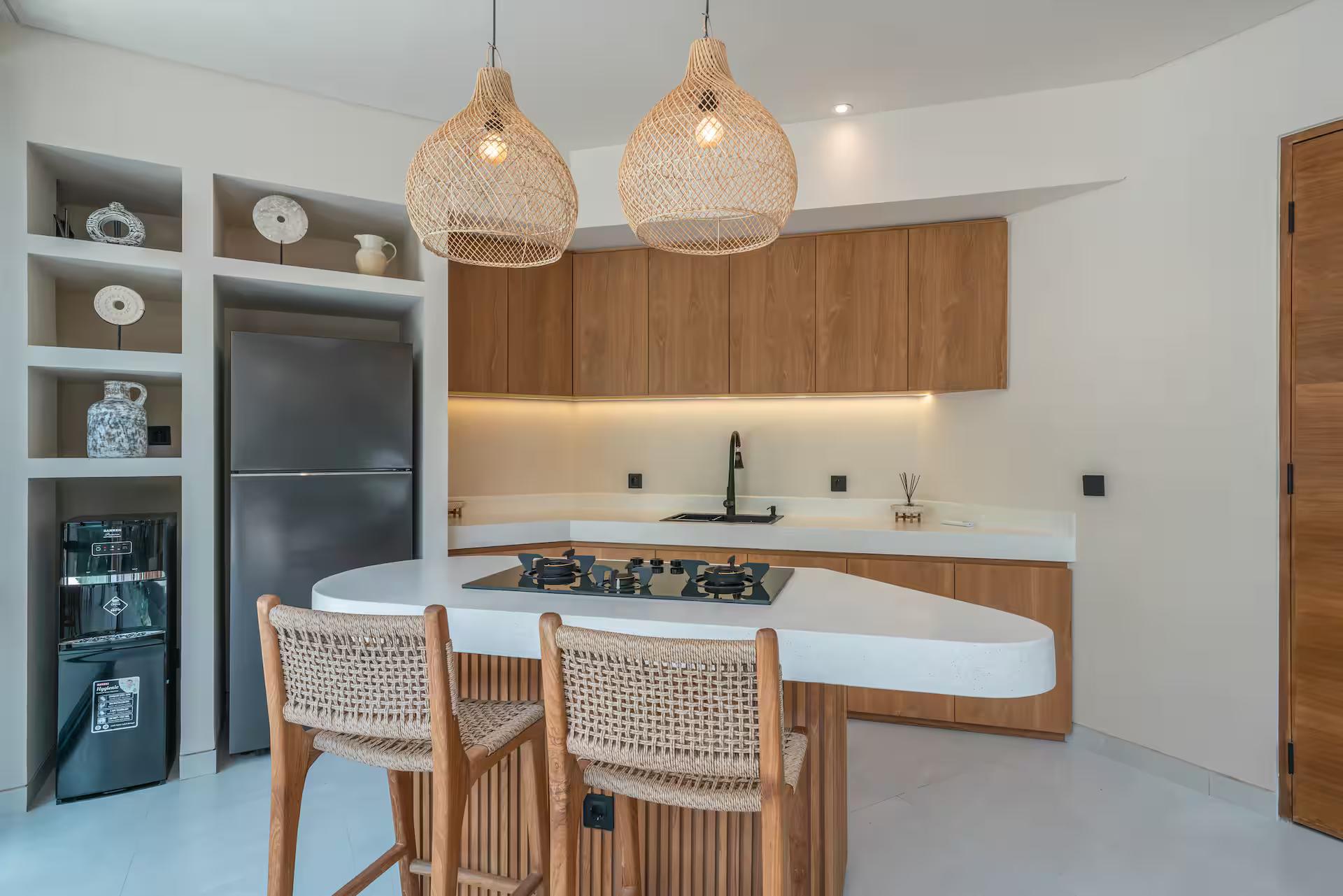 Curved white stone kitchen island with a gas hob, woven bar stools and rattan basket pendants