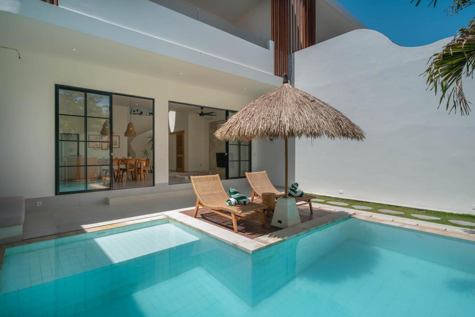 The timber sun deck set into the pool at Villa Yuri, palms above the white wall