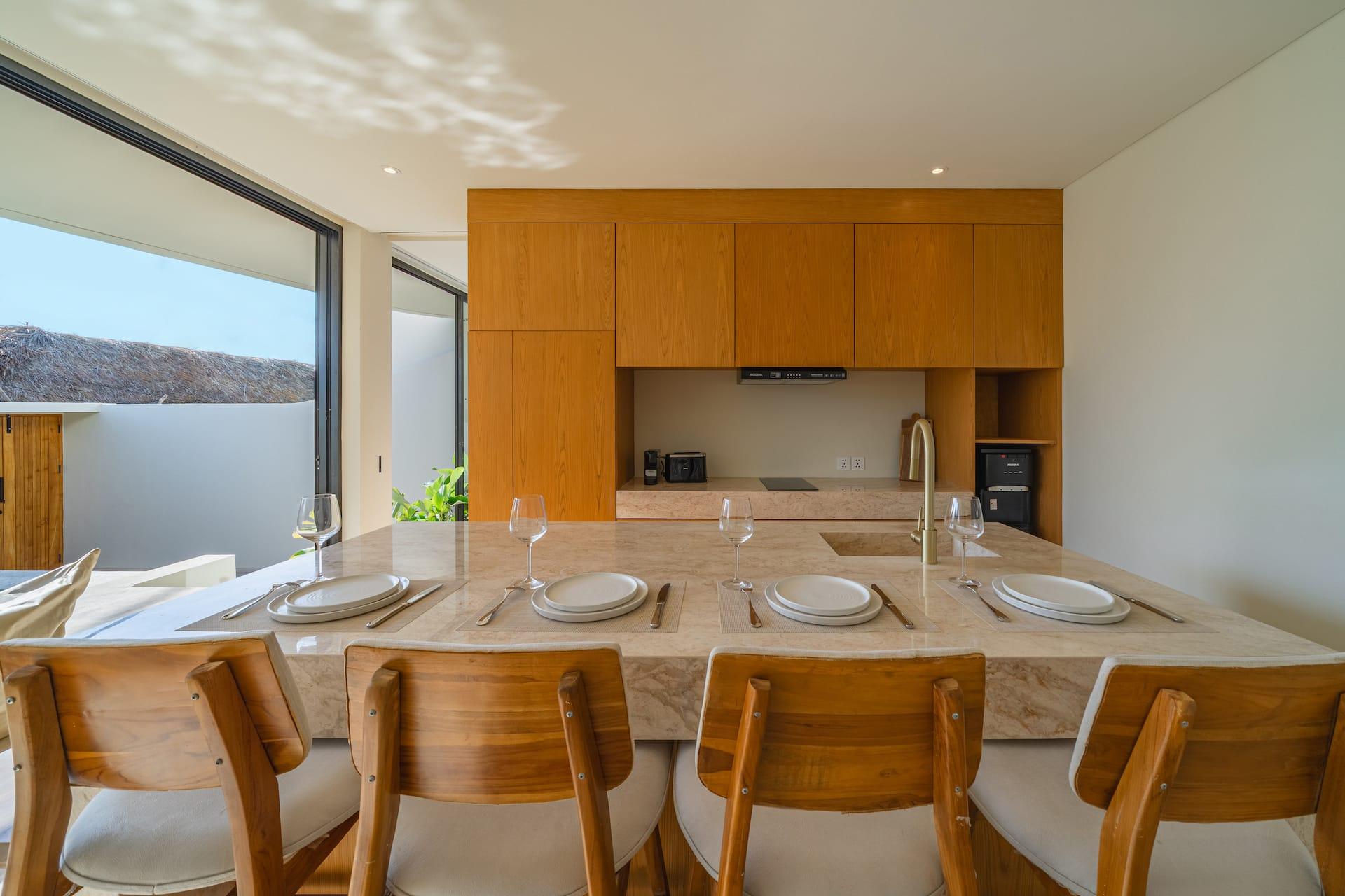Travertine island at Villa Amber laid for six with timber stools and the kitchen joinery behind