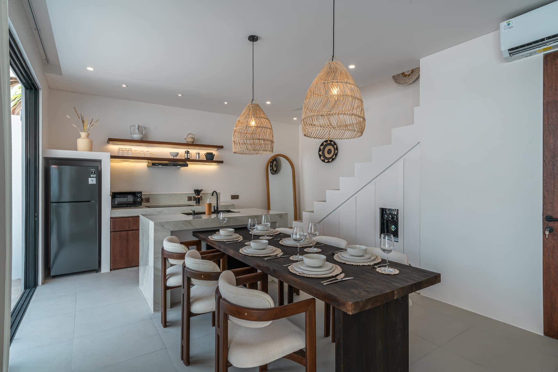 Timber dining table for six under rattan pendants, kitchen and open stair behind