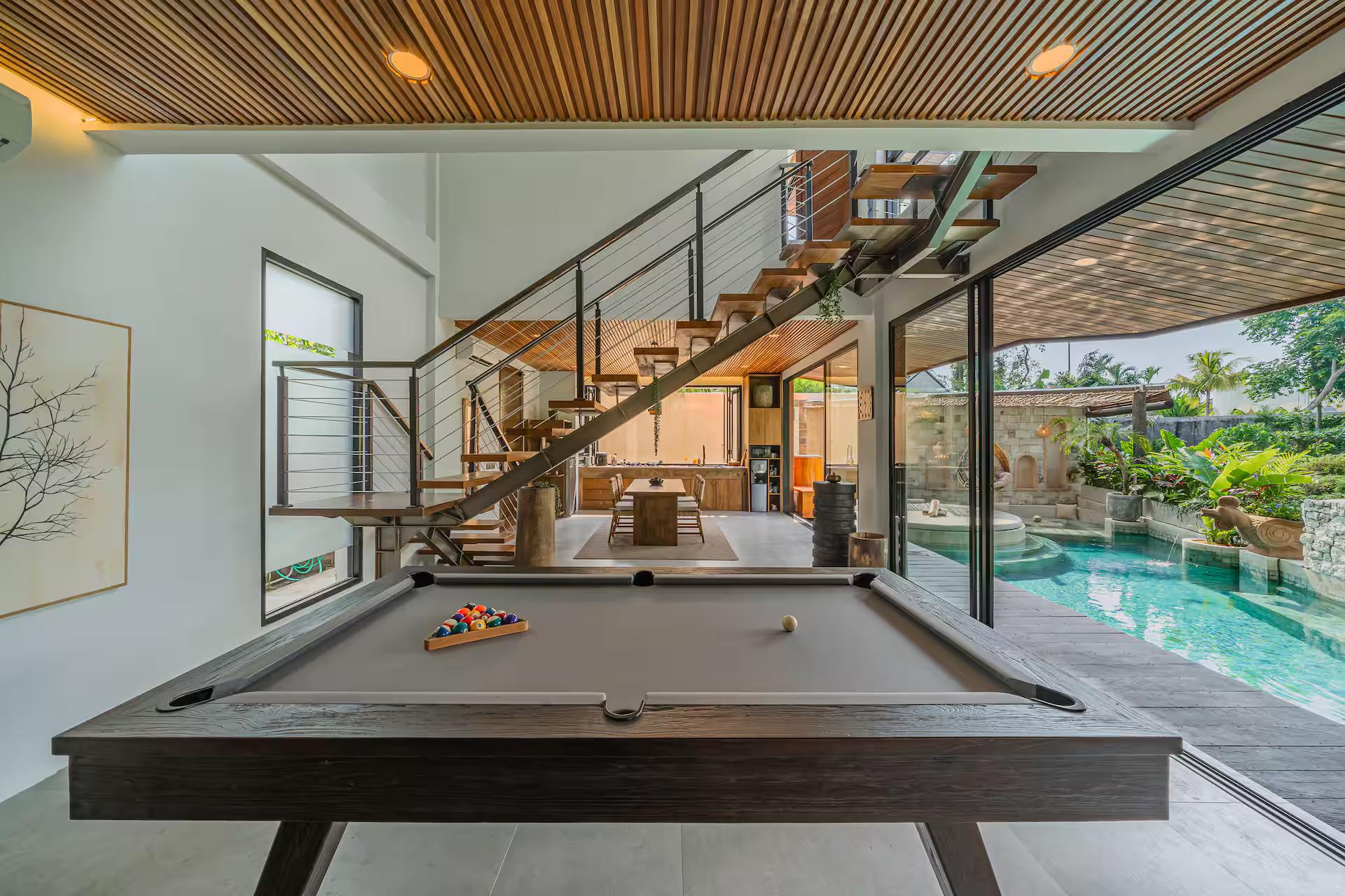 The pool table set under a timber-slat ceiling, the pool visible through the glass