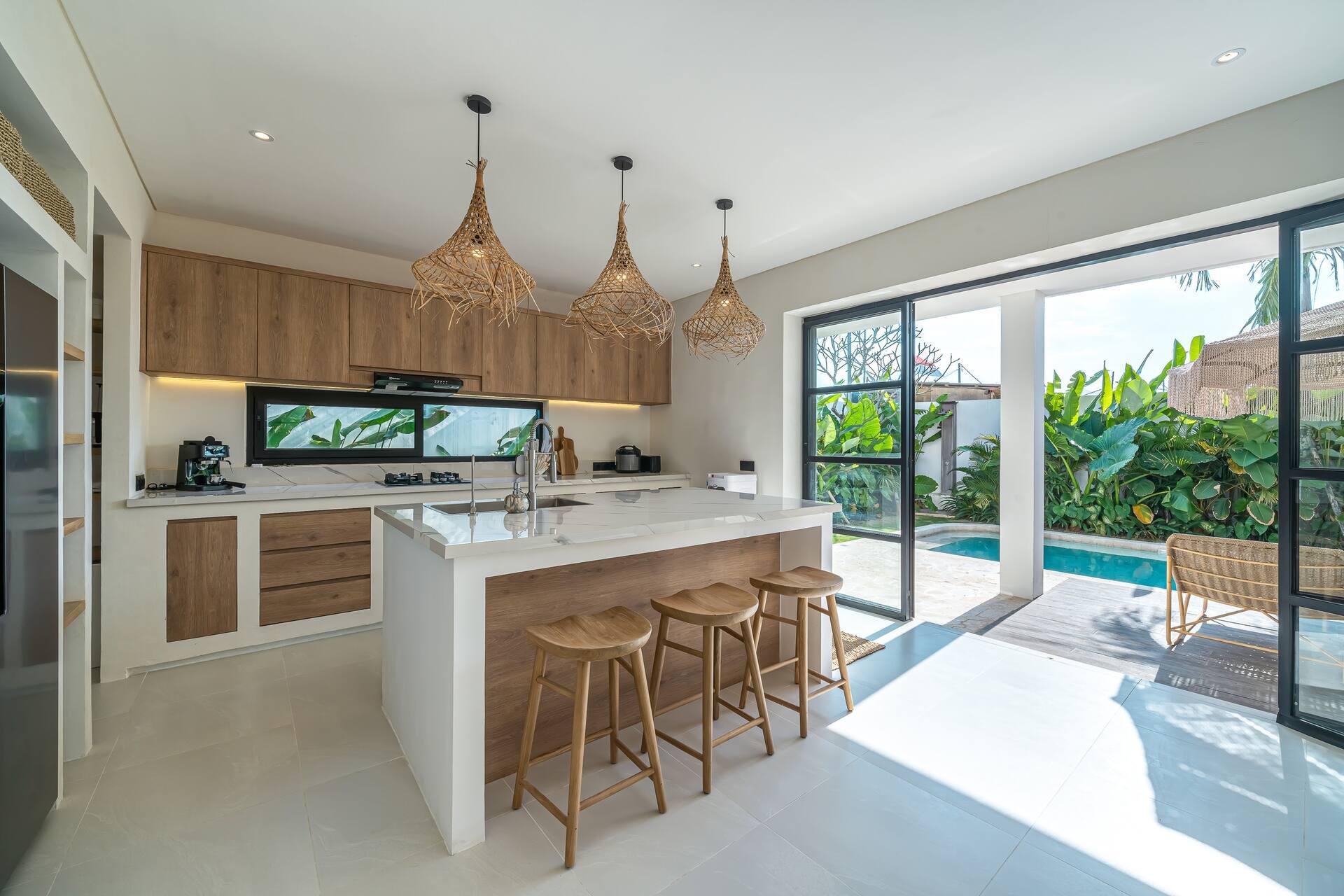Kitchen island in white stone with rattan bar stools, glass doors open to the pool terrace