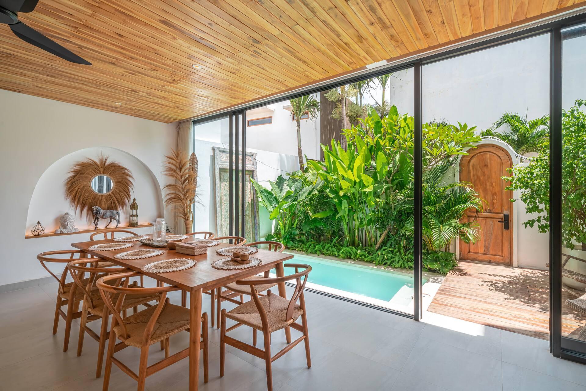 Dining table for eight with wishbone chairs beside glass walls opening onto the pool and garden