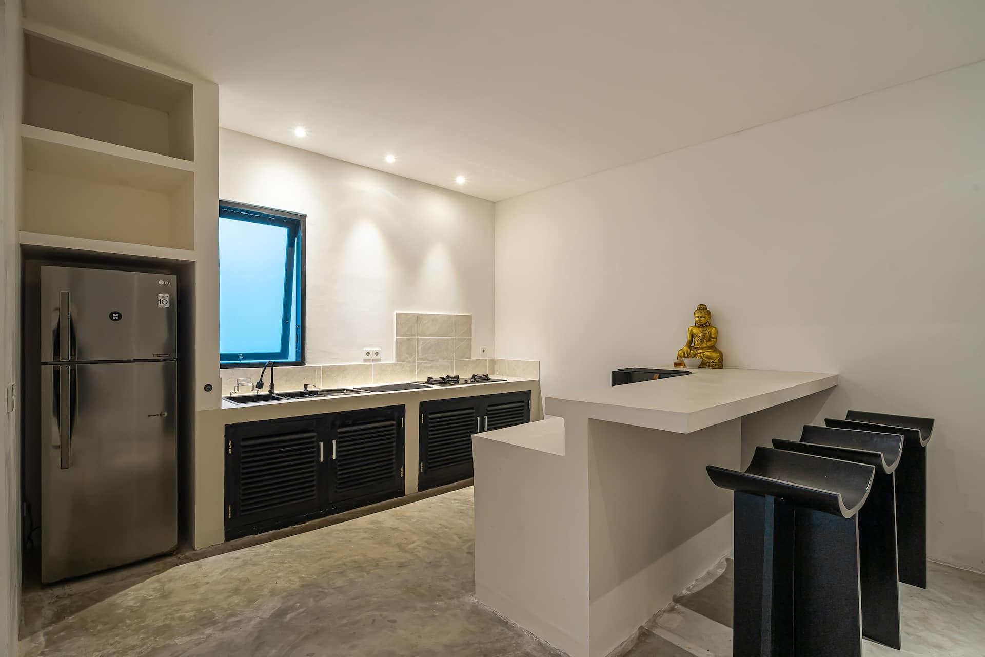 Kitchen with dark cabinetry, a white breakfast bar with black stools and a steel fridge-freezer