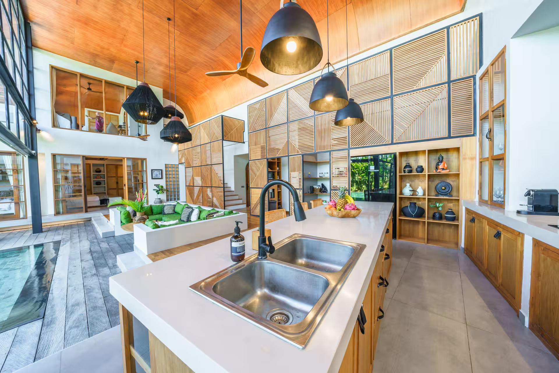 Kitchen island with sink and black pendants under the curved timber ceiling