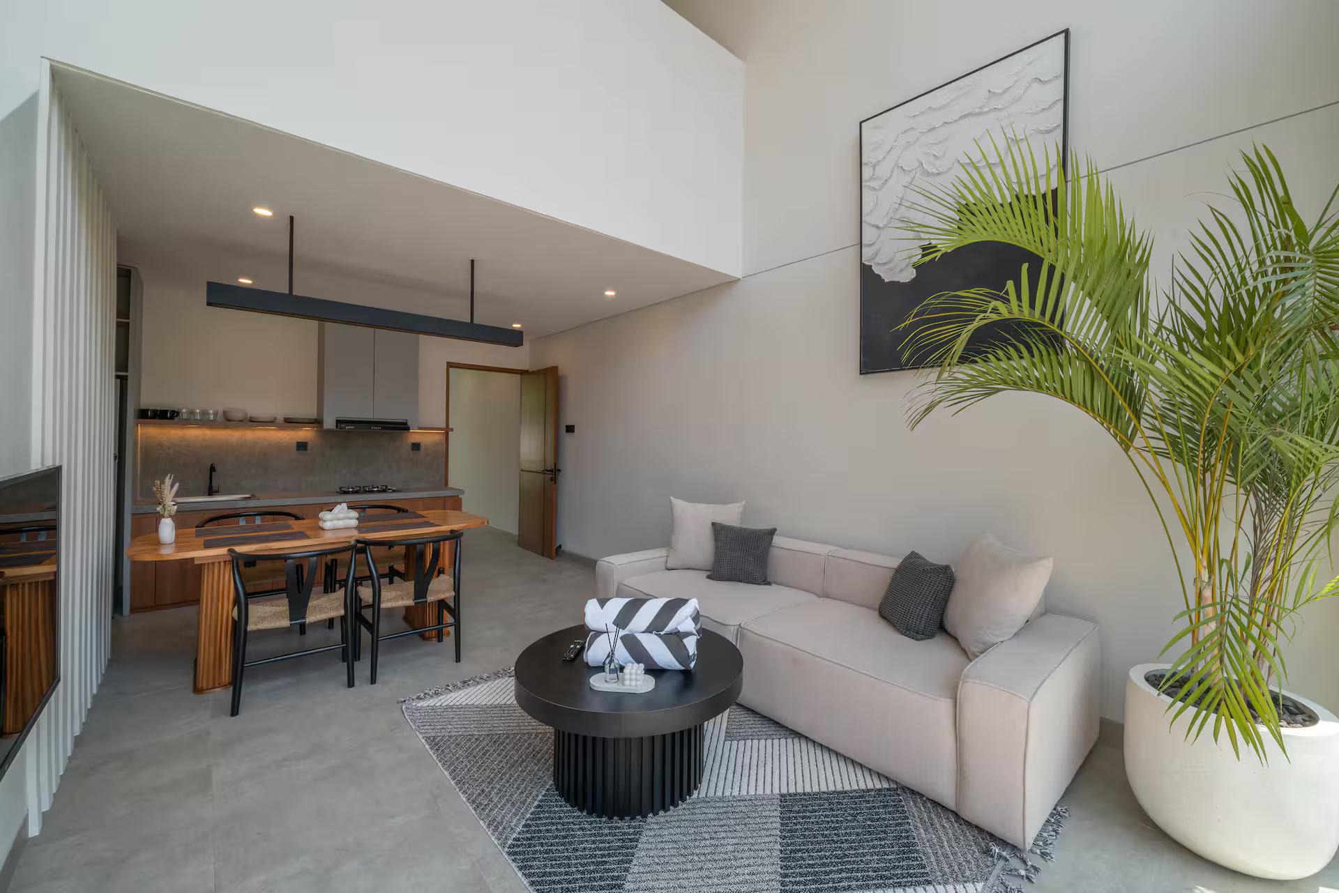 Living room and kitchen seen from the courtyard side, a palm beside the sofa