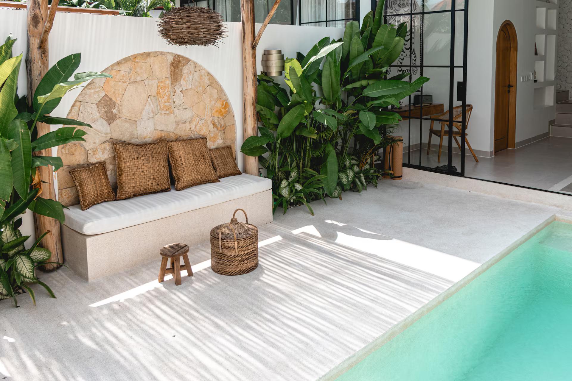 The thatched alcove and cushioned daybed seen down the length of the pool at The Macan Canggu