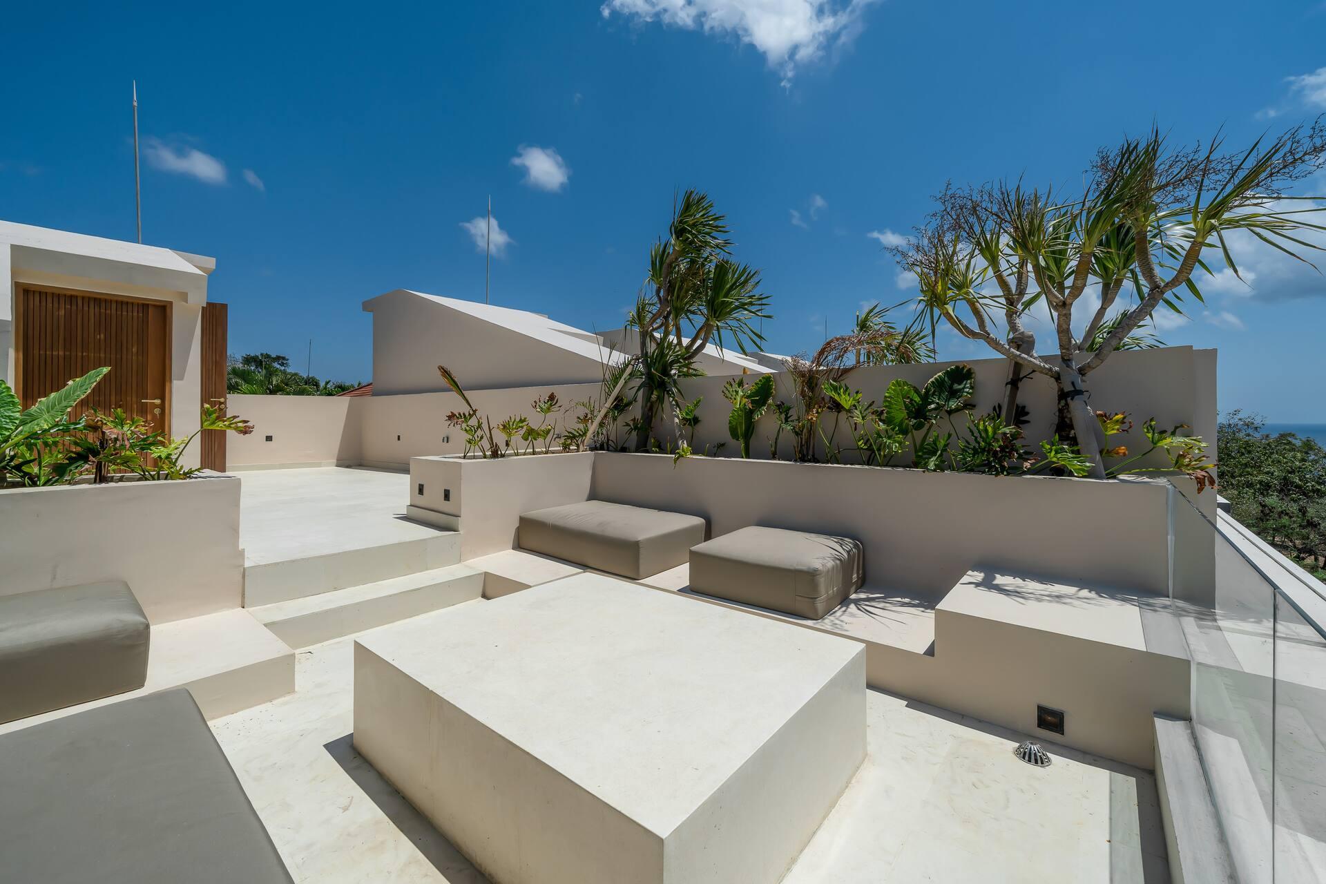 Rooftop terrace with a stone lounge platform, cushioned seats and planters edged by a glass balustrade