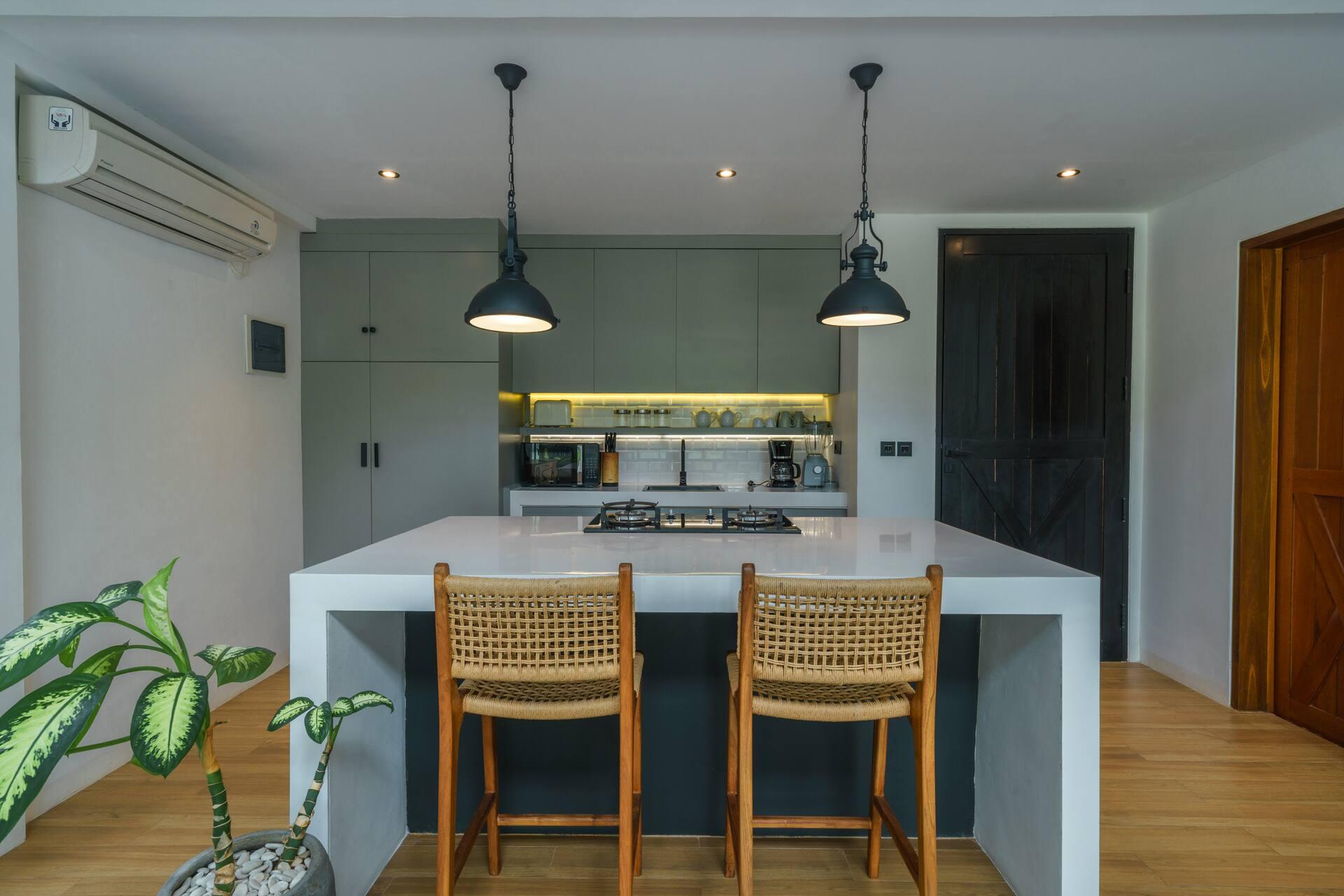 Kitchen island with rattan bar stools, sage-green cabinetry and a warm lit shelf of glassware