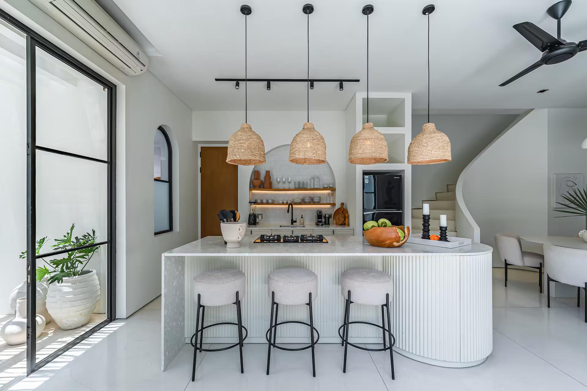 White kitchen island with black-legged stools under woven rattan pendants
