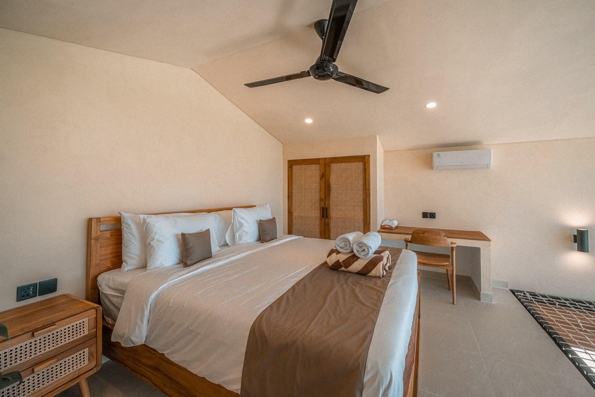 The second bedroom with a ceiling fan, a timber desk and a cane bedside table
